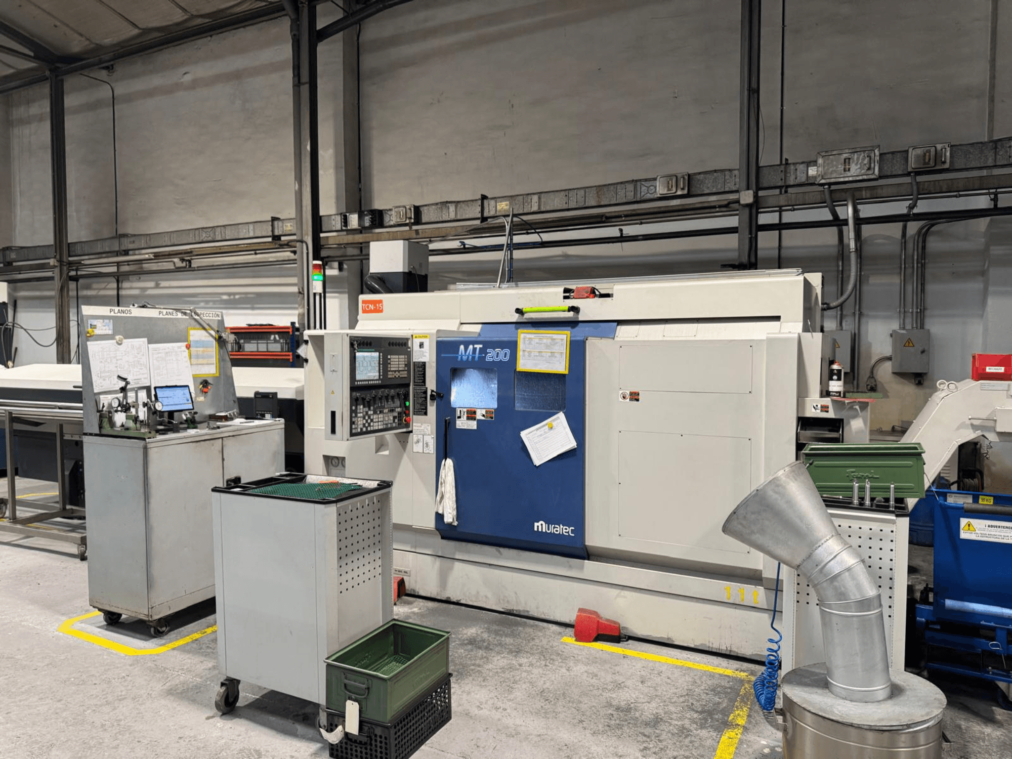 Muratec MT200 multi-spindle turning machine in a factory setting, viewed from the front, with control panel and surrounding equipment.