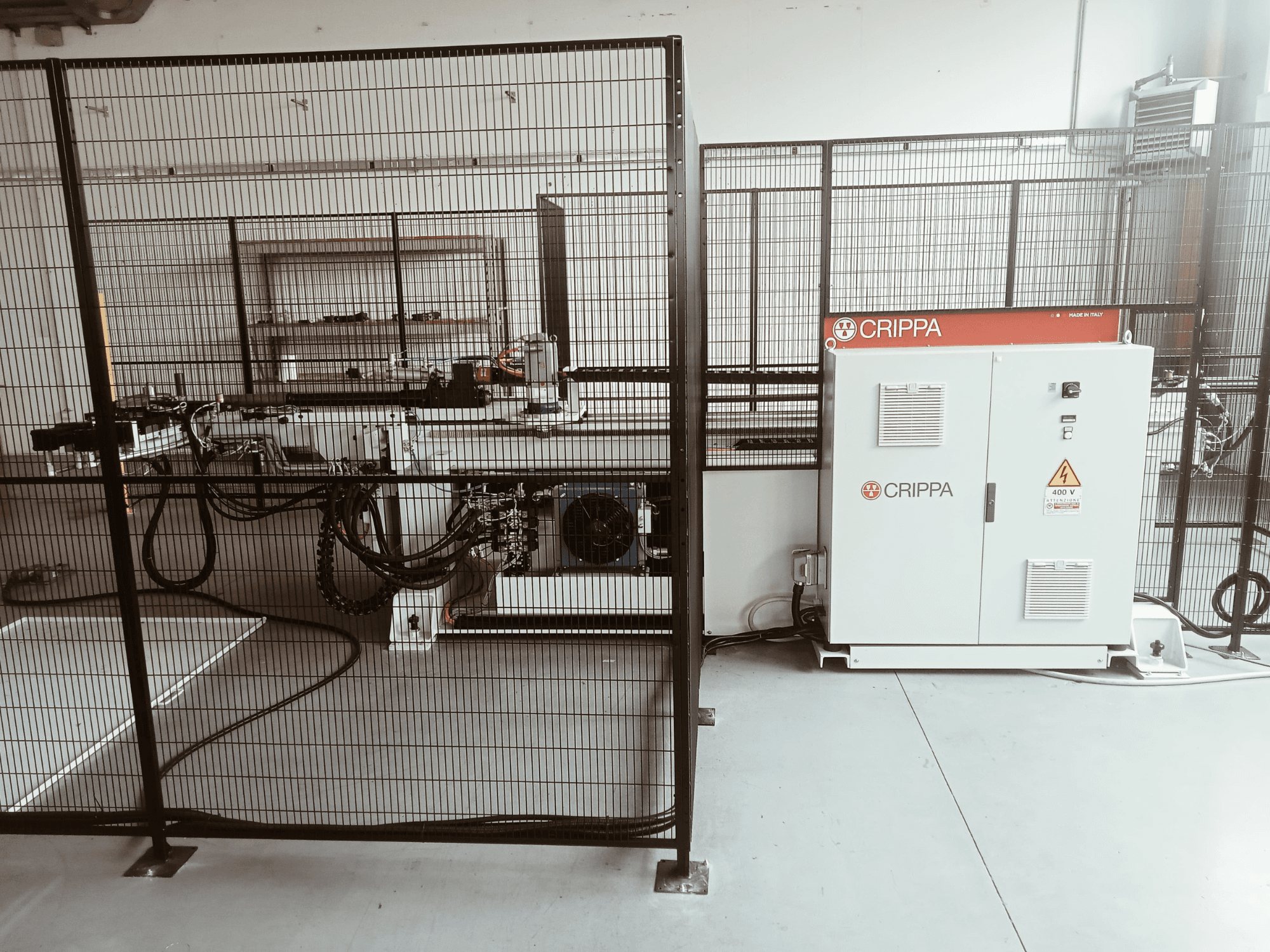 White CRIPPA machine behind a safety cage, with visible hoses and components, side view, industrial setting.