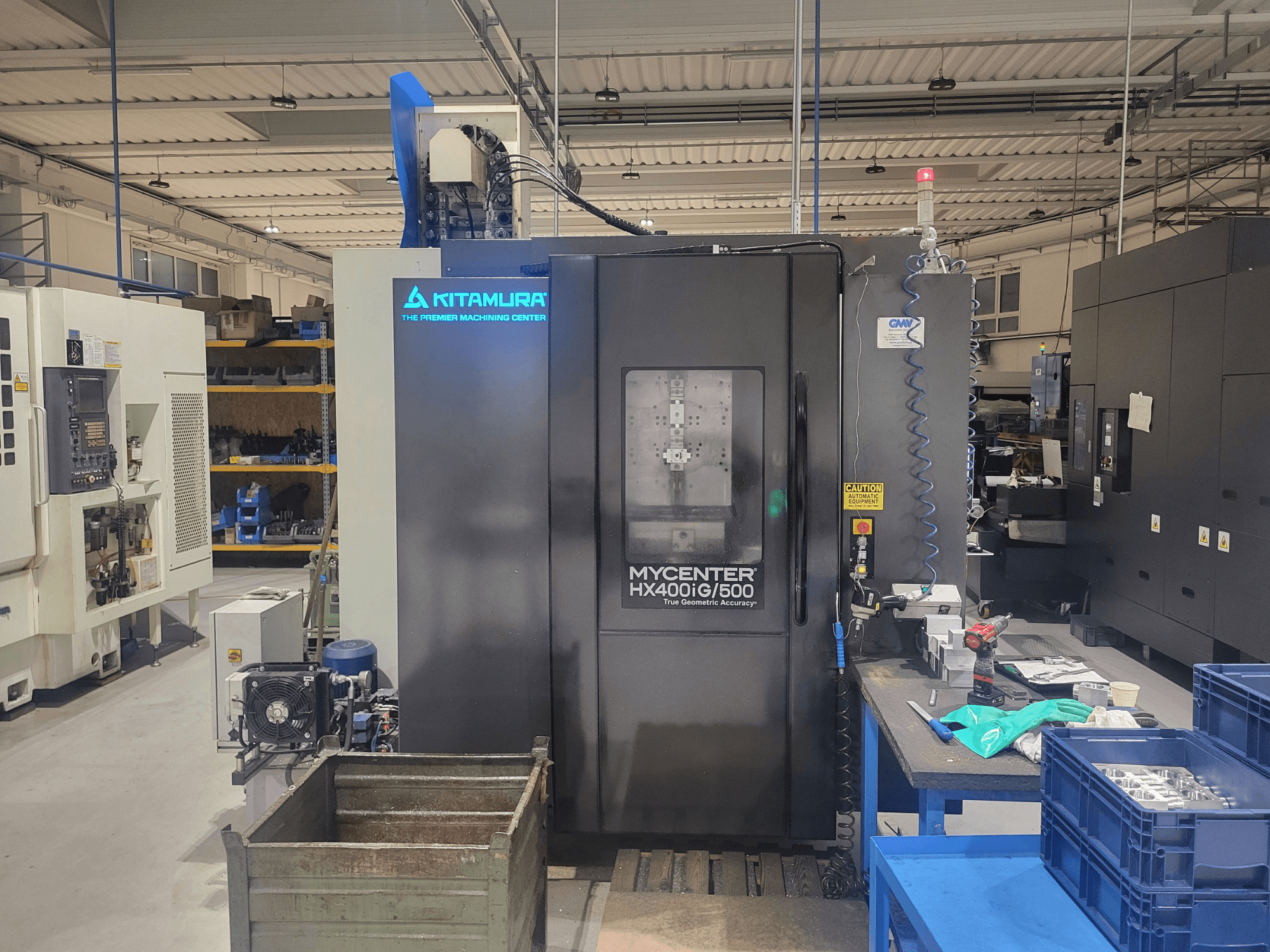 Kitamura Mycenter HX400iG/500 CNC machine in a workshop, front view, with controls, tool storage, and materials nearby.