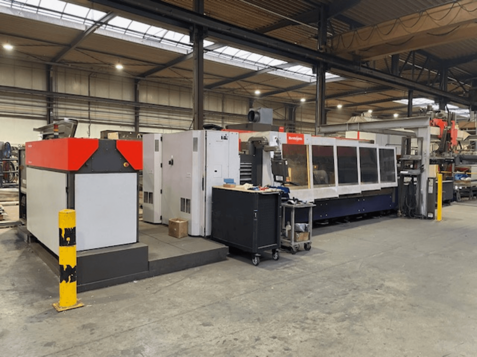 Bystronic BySpeed 3015 CO2 laser cutting machine, side view in a workshop, featuring distinct red and gray design elements.