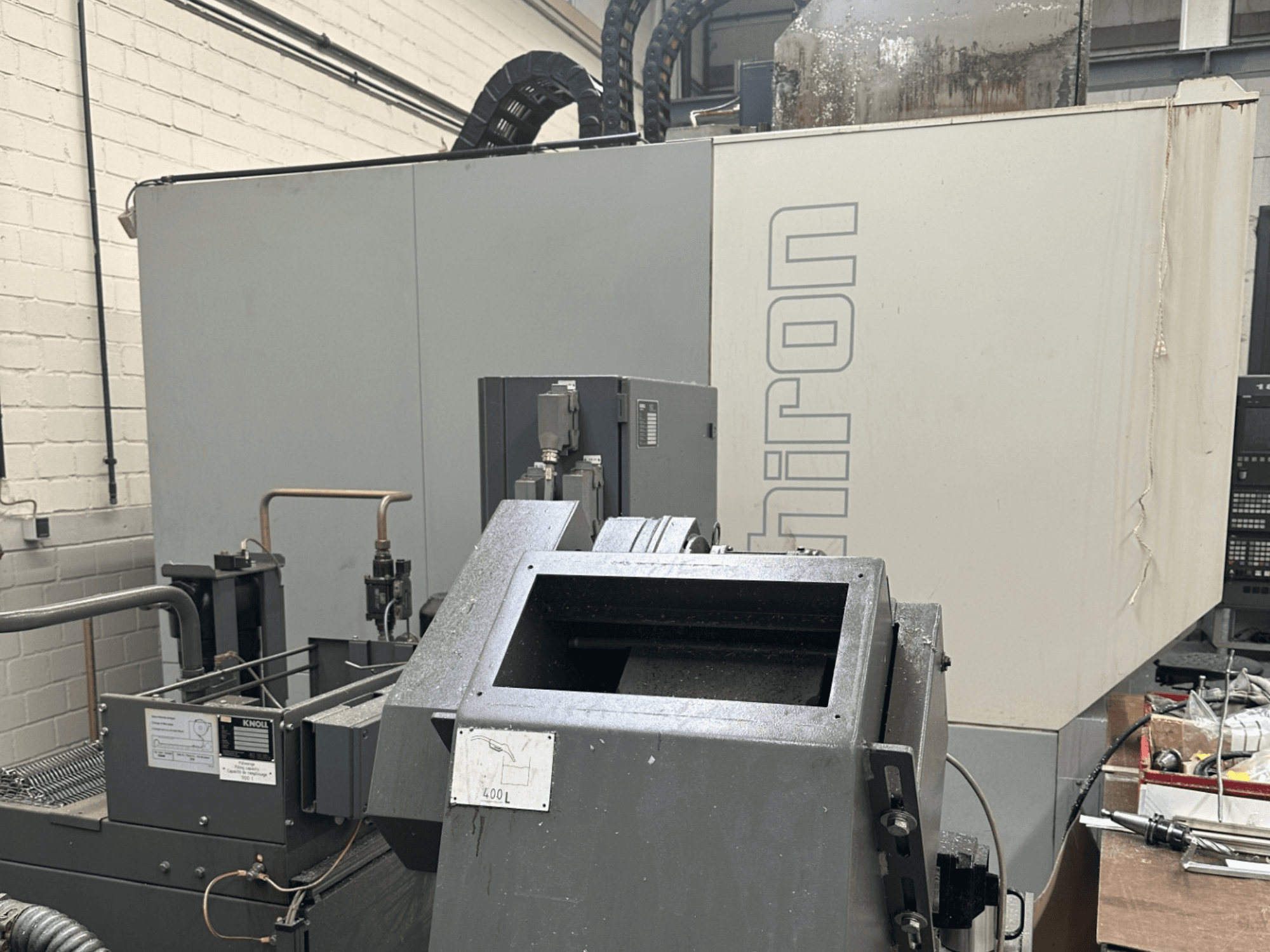 BRAND: Chiron; Front view of industrial CNC machine with gray exterior, control panel visible, and machinery components in focus.