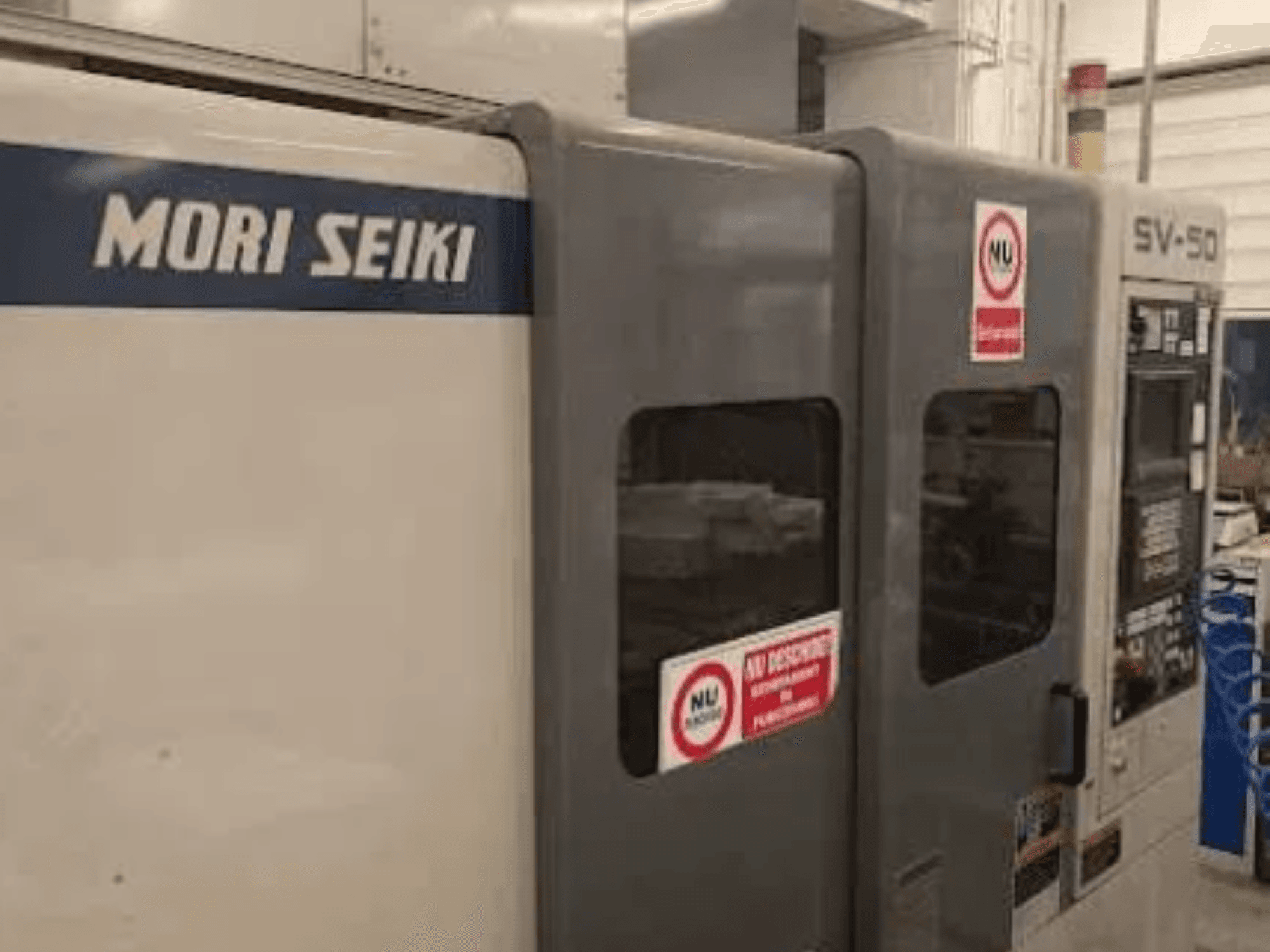 MORI SEIKI SV-50 CNC machine, side view; features control panel and safety warning stickers.
