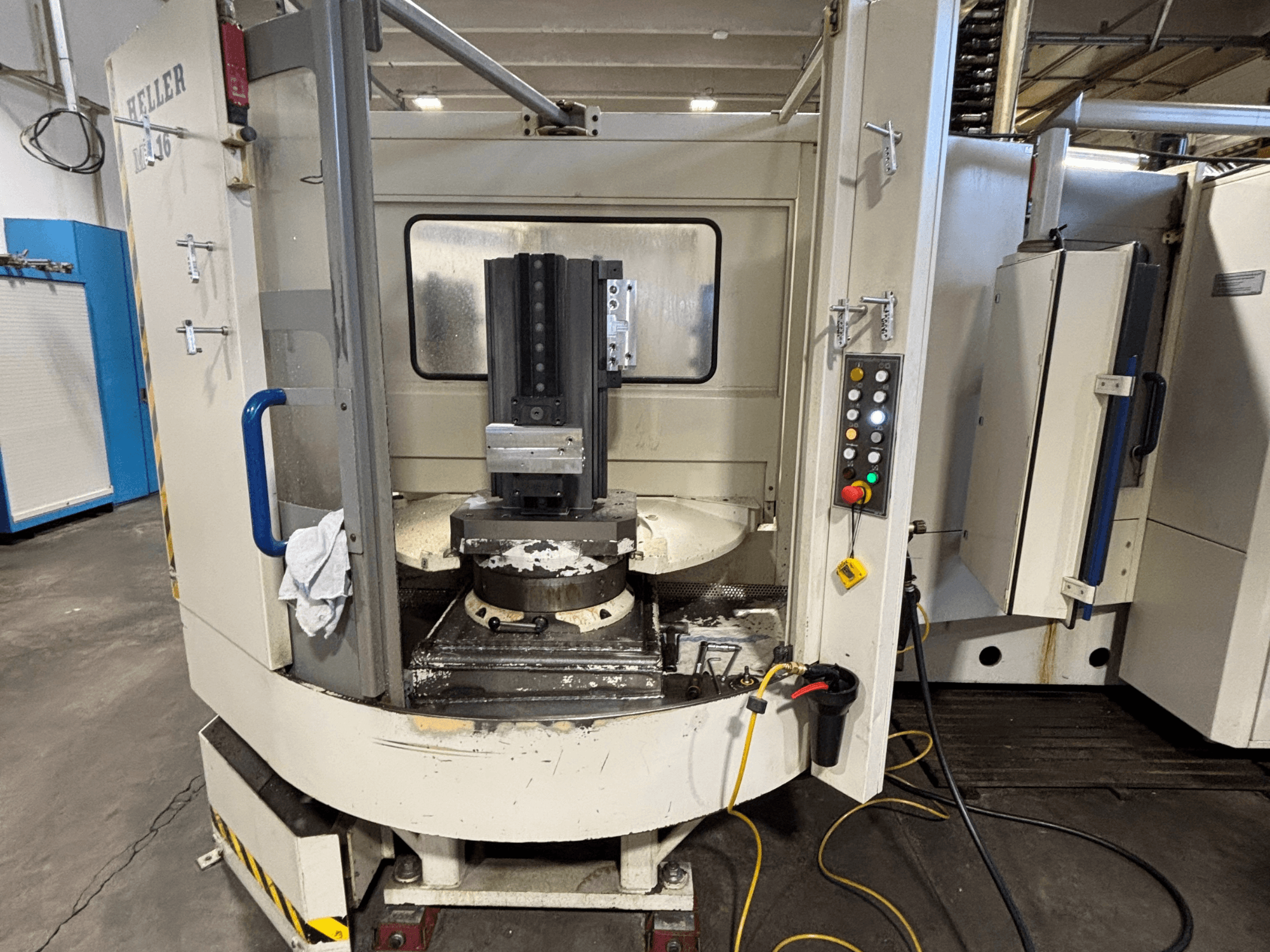 Heller machining center, model vertical, front view showing spindle, control panel, and worktable with equipment attached.