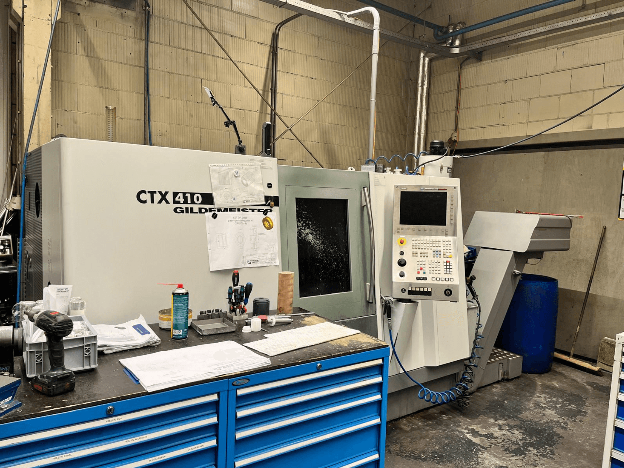 Gildemeister CTX 410 CNC machine in a workshop, front view, featuring a control panel and various tools on a workbench.