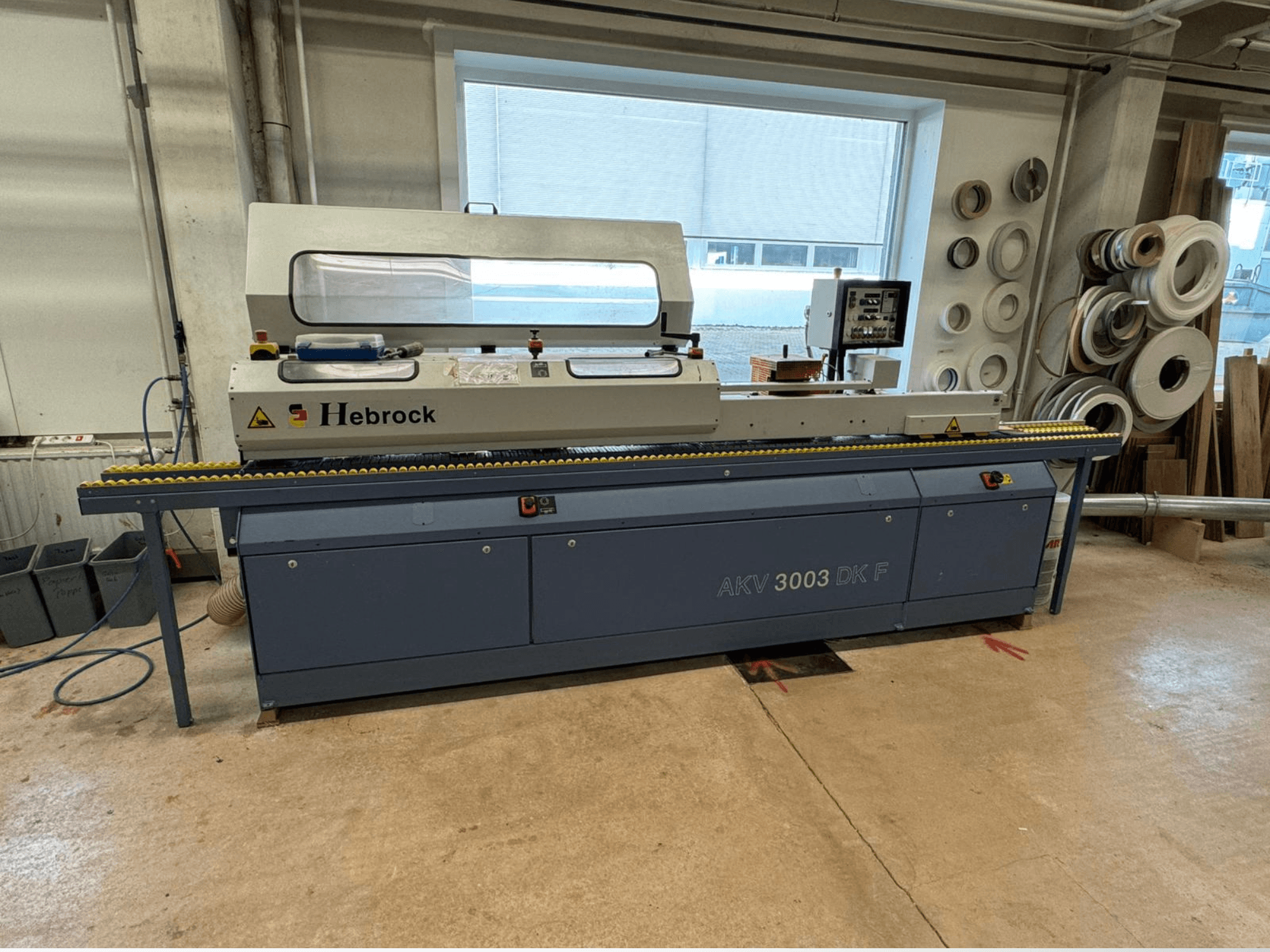 Hebrock AKV 3003 DK F edge banding machine, front view, features a conveyor and control panel, situated in a workshop.
