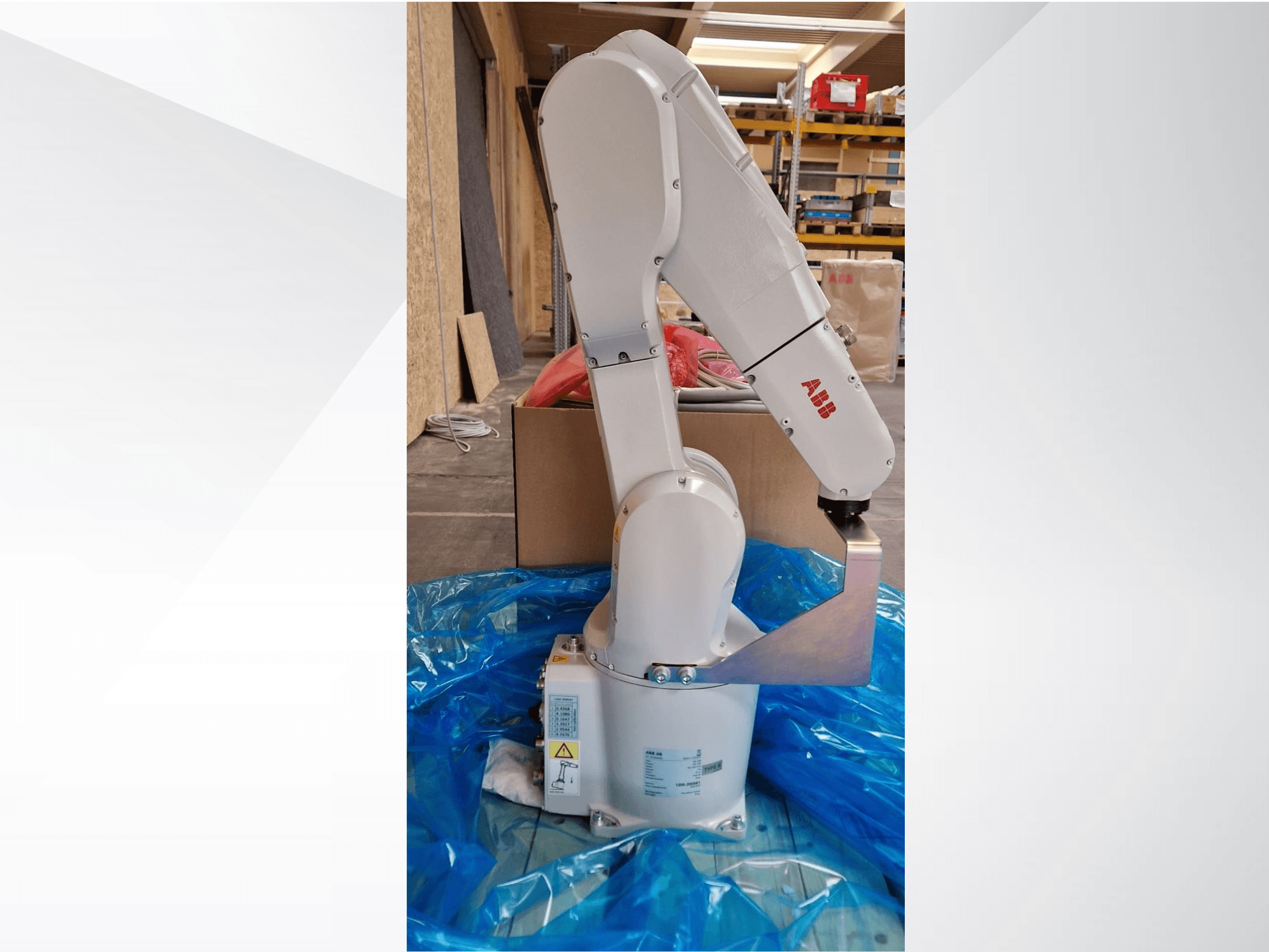 ABB robotic arm model, side view on blue tarp, showcasing articulated joints and metal end effector, with technical labels visible.