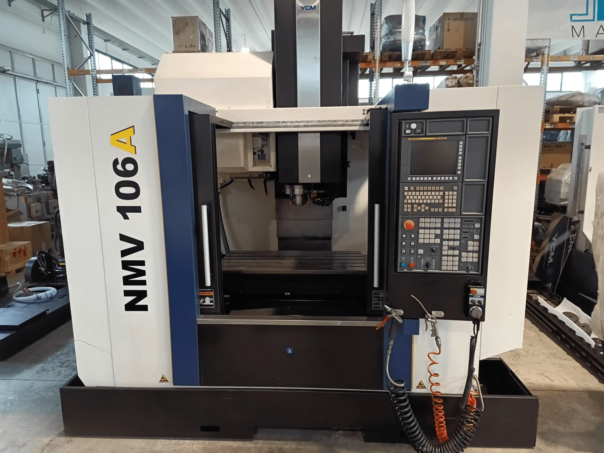 YCM NMV 106A machining center, front view, featuring control panel with buttons and coolant hoses.