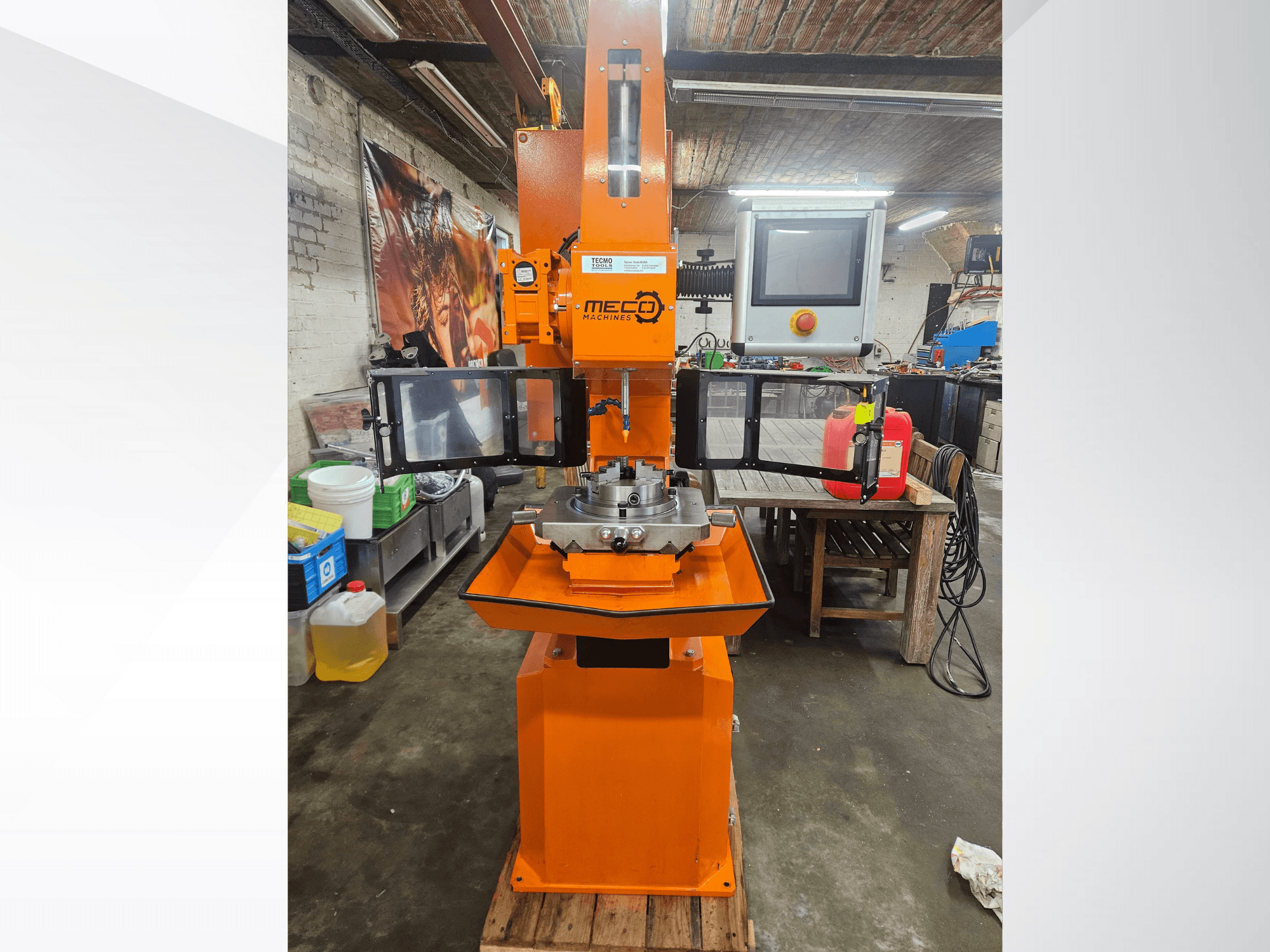 MEC orange milling machine, front view, with control panel and worktable, located in a workshop with tools and materials.