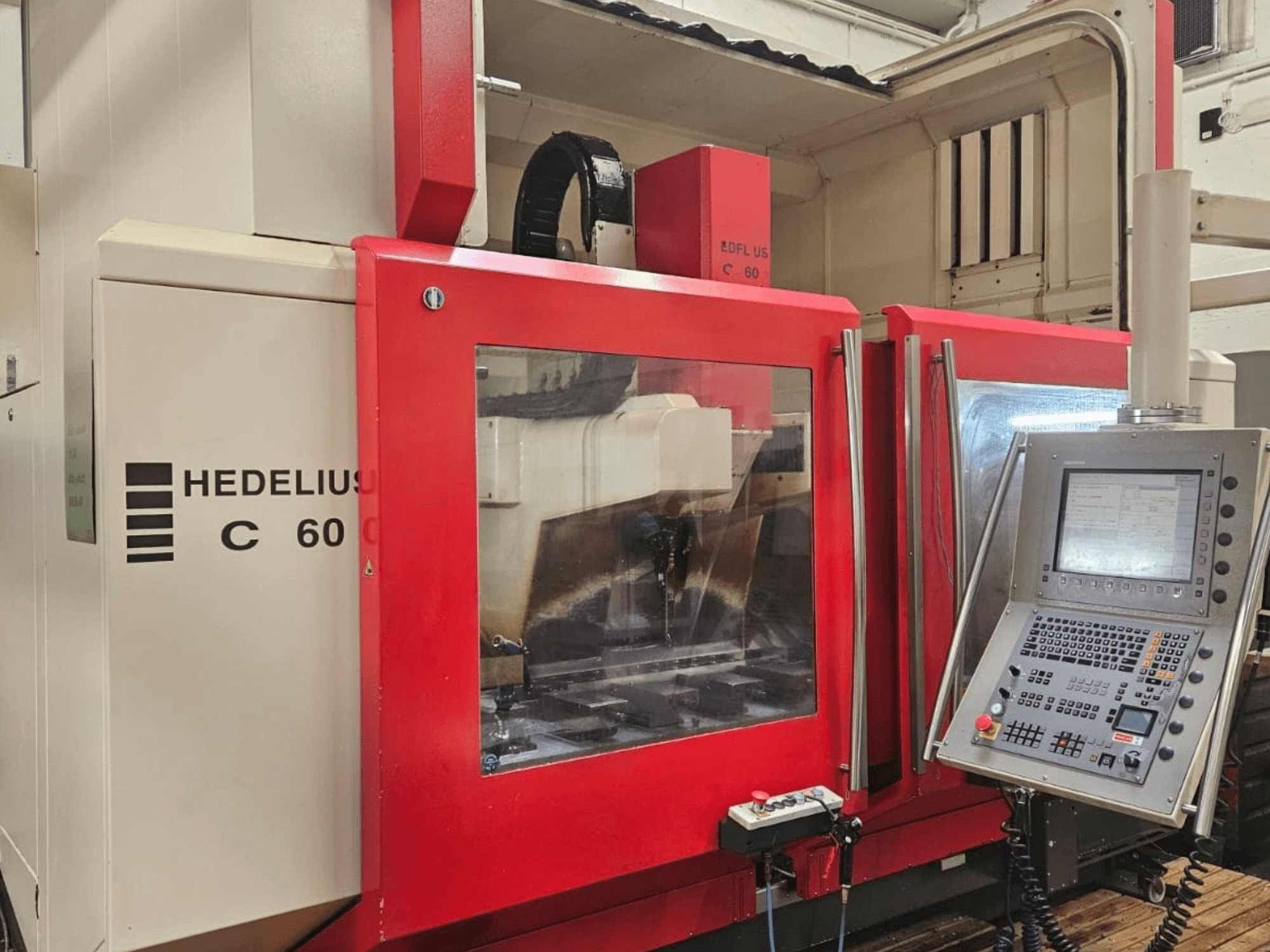 HEDELIUS C60 vertical machining center from the side, featuring a red front panel and control console with display.