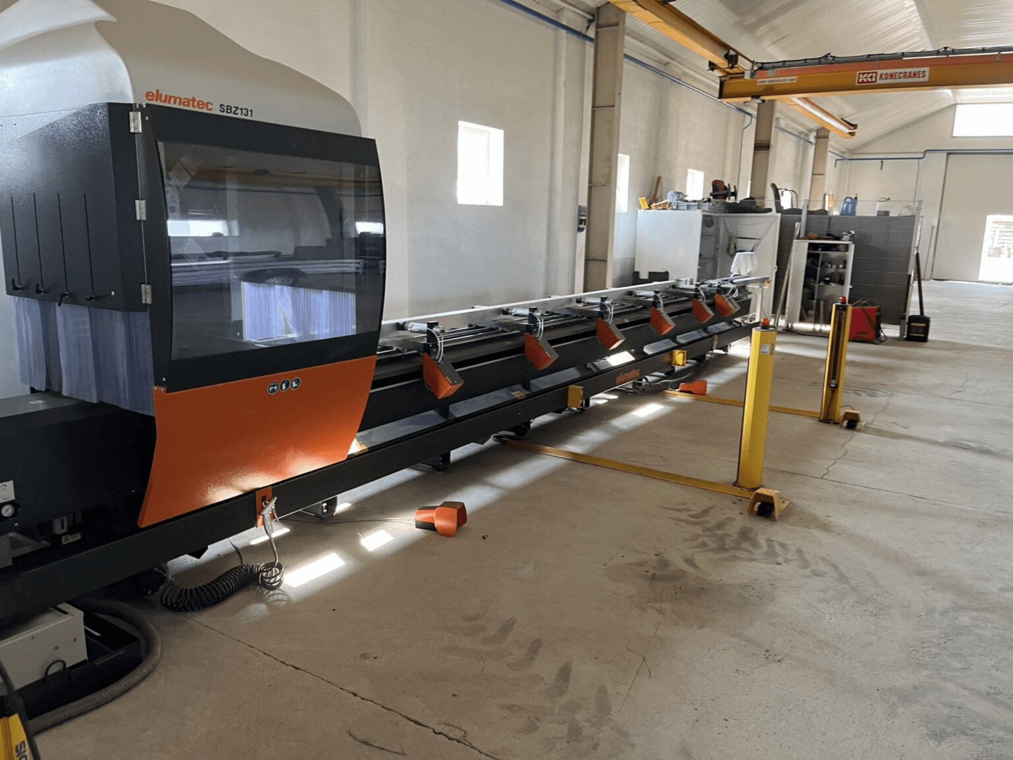 Elumatec SBZ131, front view of a linear milling machine with orange and black design, in a workshop setting.