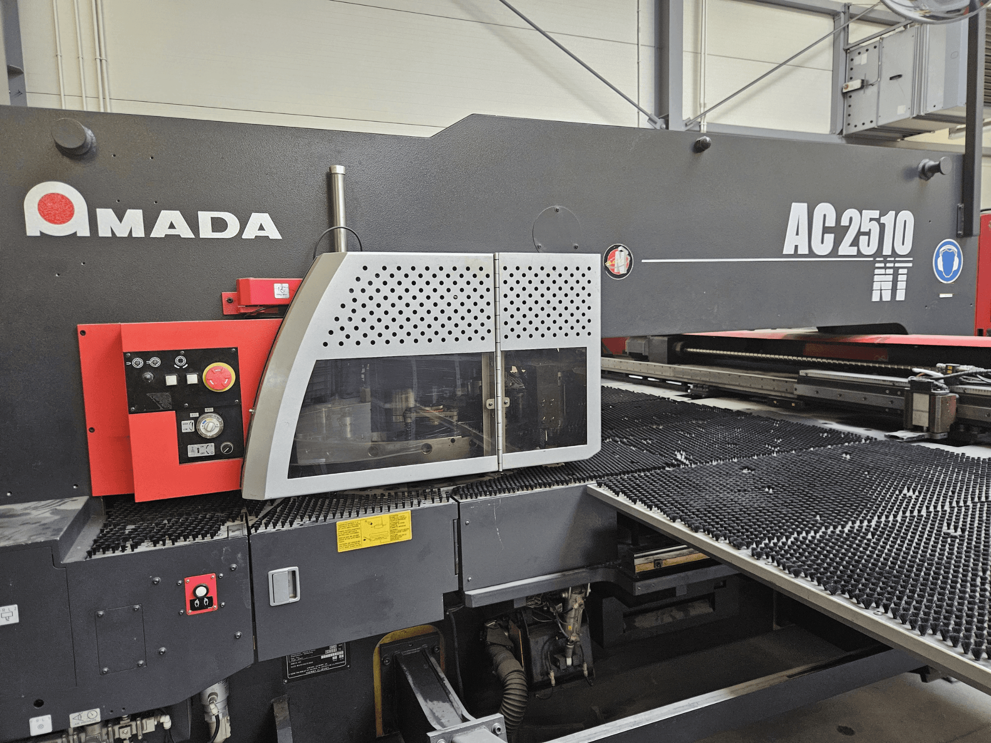 Amada AC2510 NT laser cutting machine, front view, featuring control panel with knobs, buttons, and a safety cover.