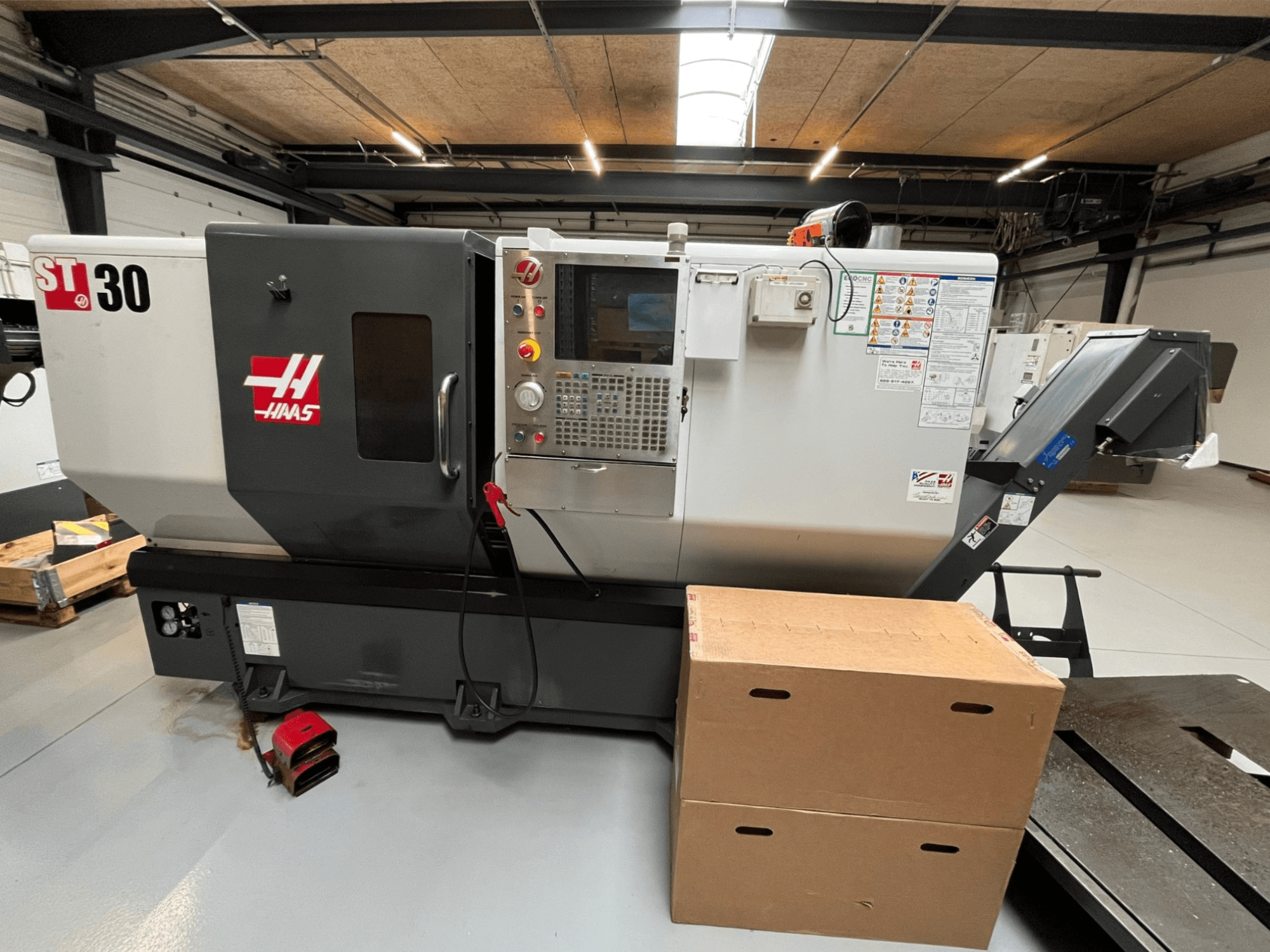 Haas ST-30 CNC lathe, front view, features control panel with buttons, emergency stop, and two stacked cardboard boxes.