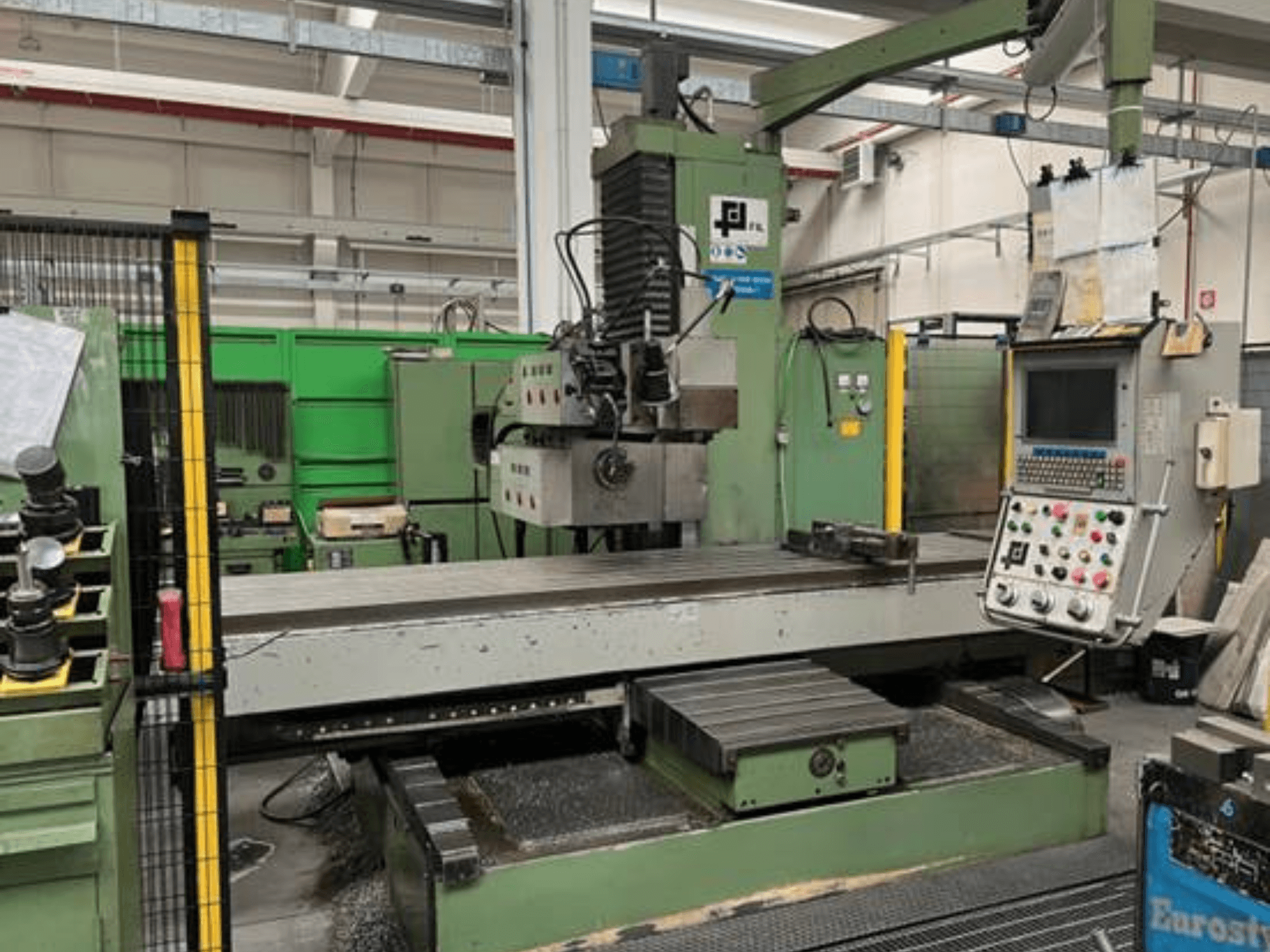 Industrial milling machine from JFL, front view with control panel, large flat table, and metal shavings on the floor.