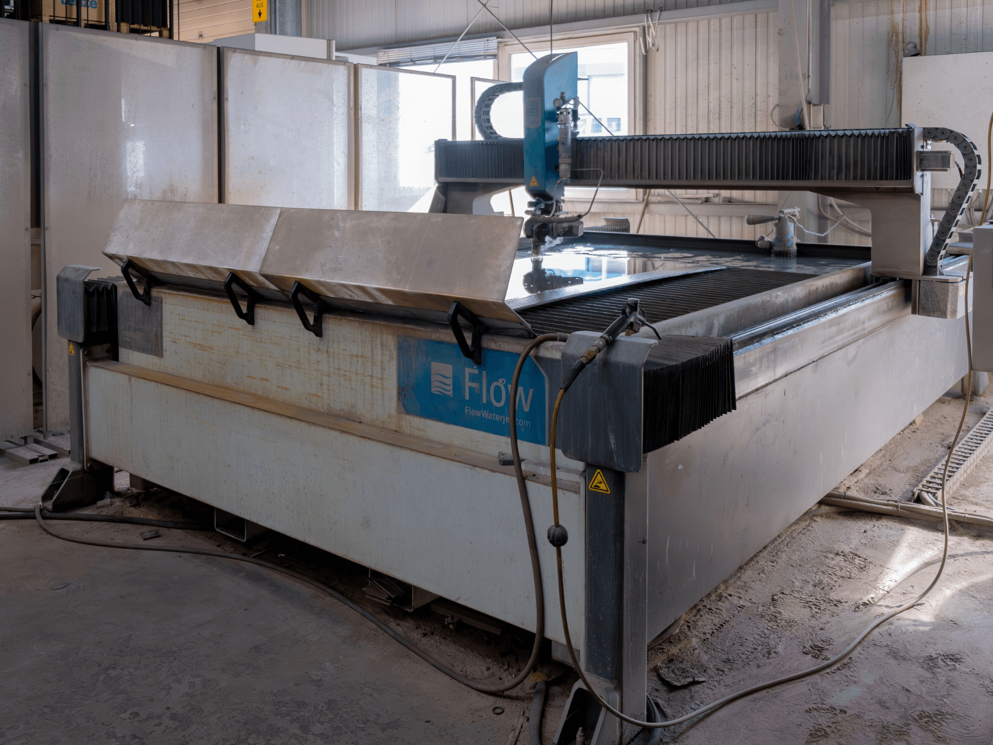 Flow KENT Mach 2 C waterjet cutting machine in a side view, showcasing the stainless steel cutting table and water jet nozzle.