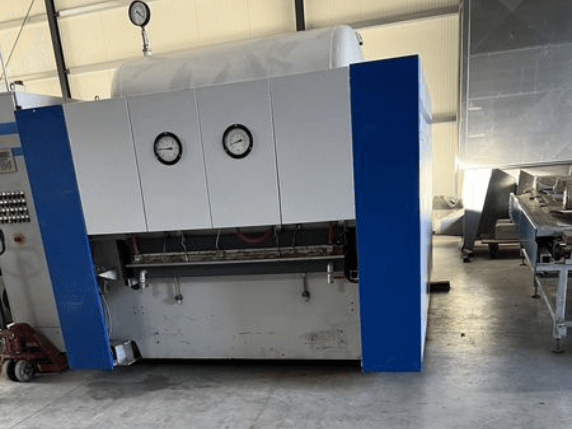 Blue and white industrial machine with two pressure gauges, front view, featuring a control panel and adjacent equipment.