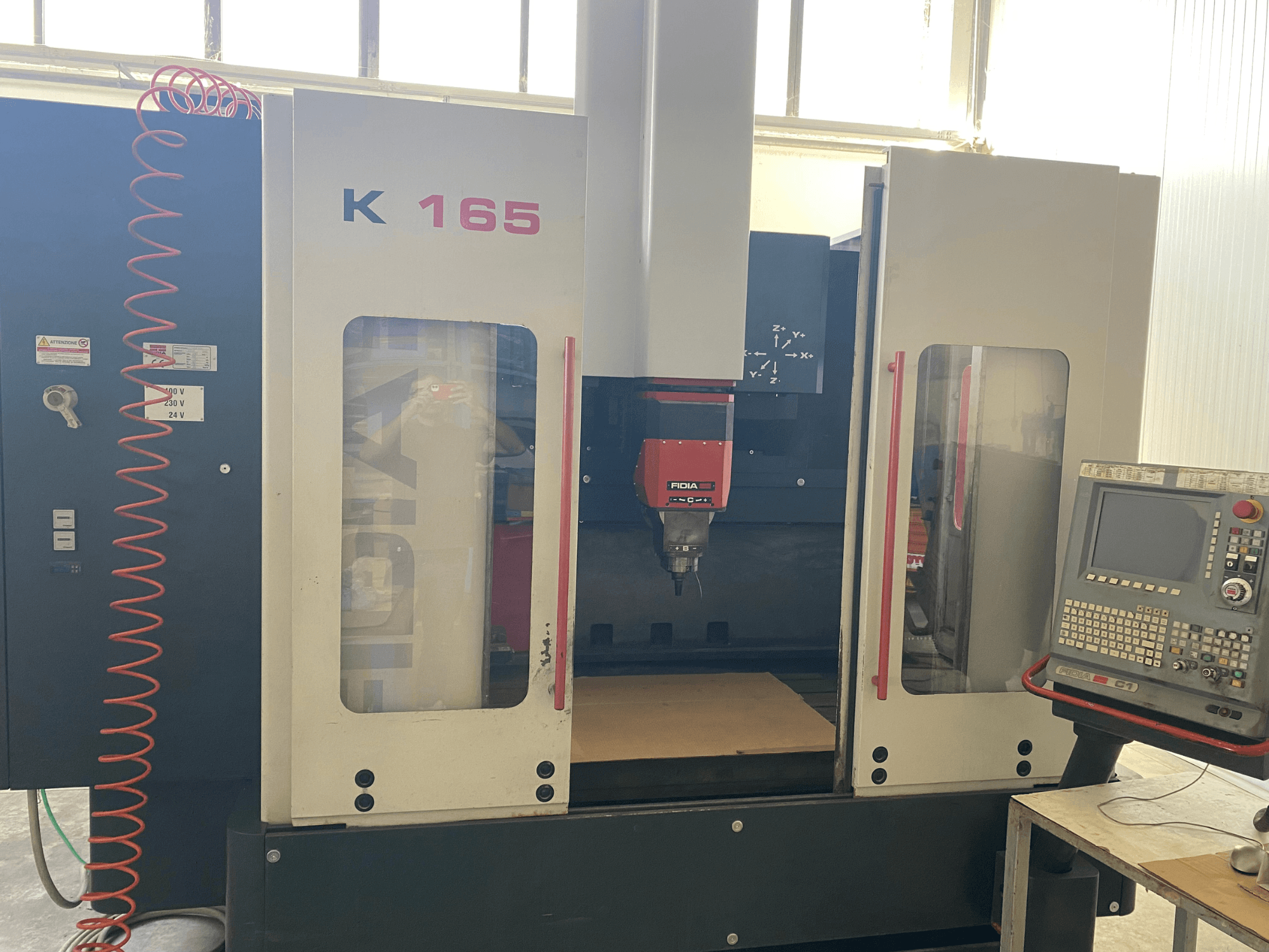 Fidia K 165 CNC machine with a red spindle and control panel, viewed from the front, in a well-lit workshop setting.