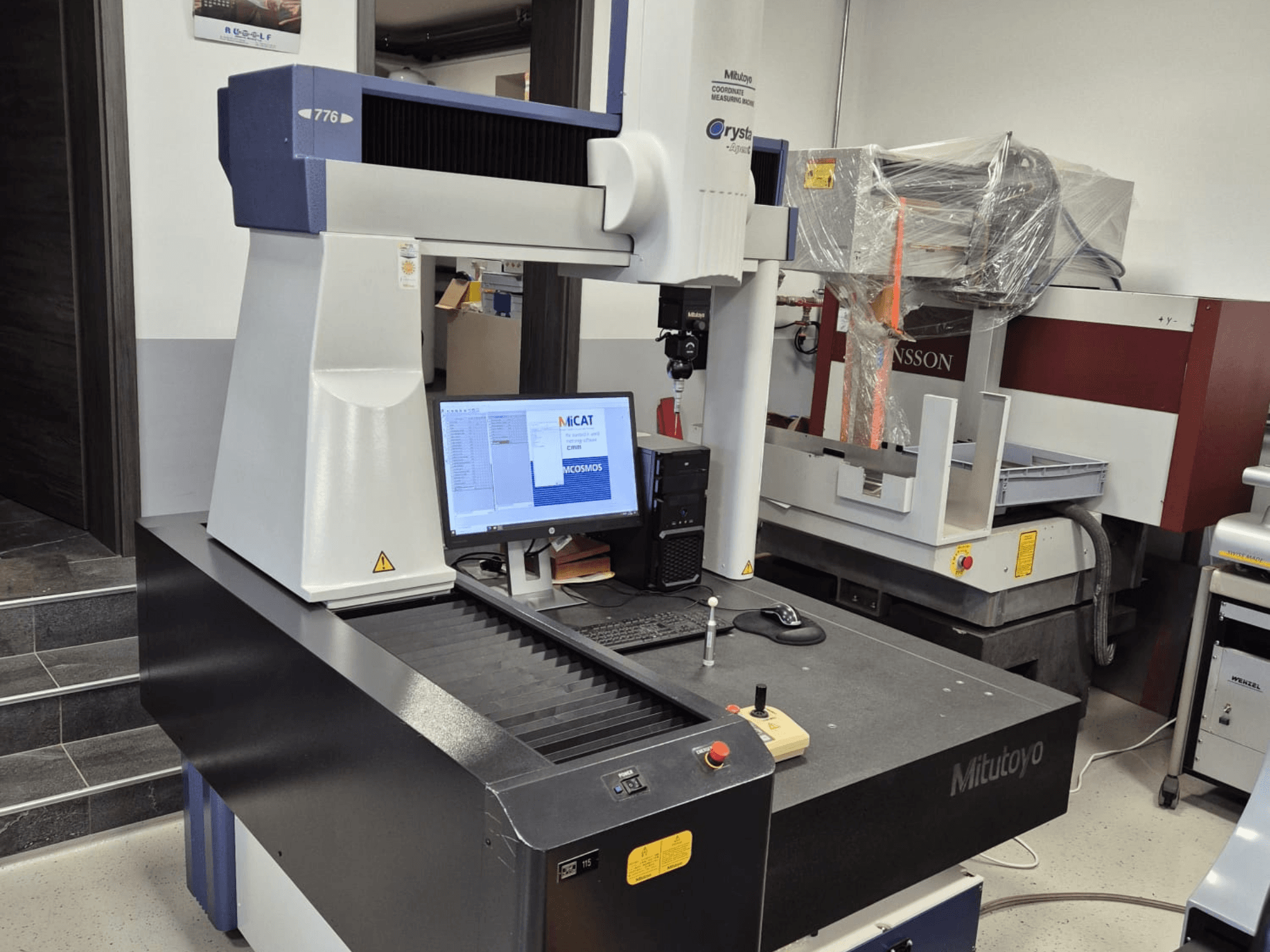 Mitutoyo model 776 coordinate measuring machine in front view, with a monitor displaying measurement software and controls visible.