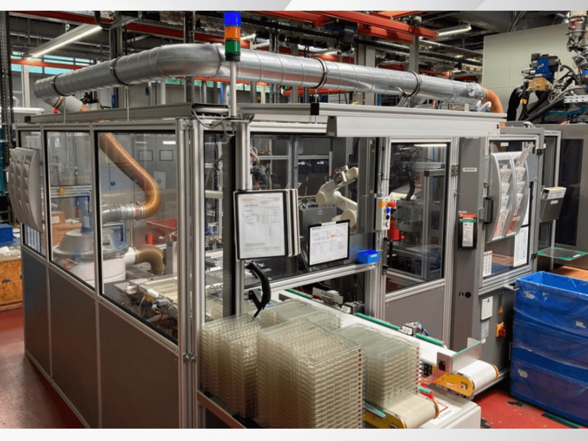 Automated assembly machine with robotic arm, transparent side panels, and stacked containers of clear items, front view.