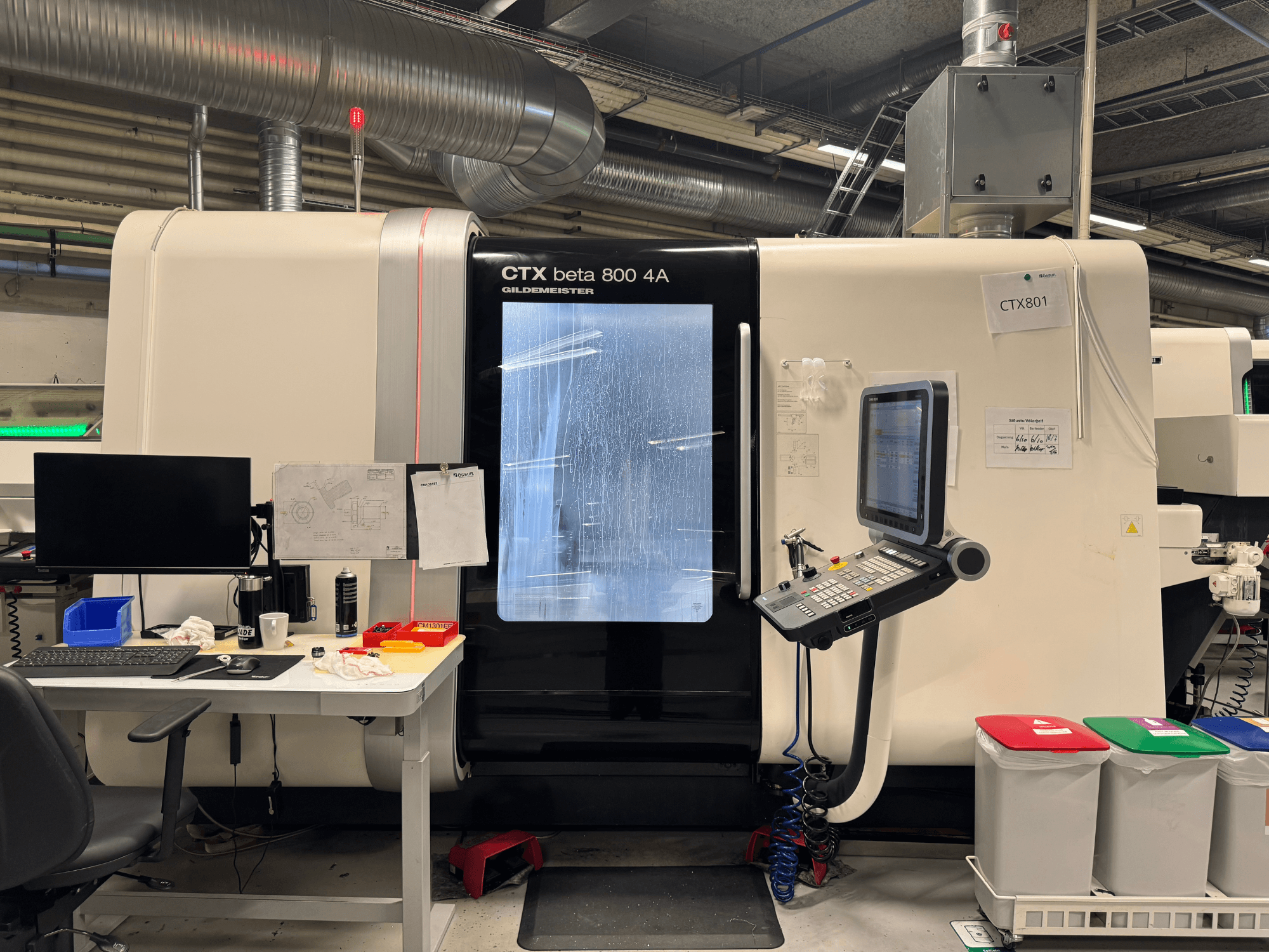 CTX beta 800 4A machine with control panel and monitor, side view, in a workshop with office setup and colored trash bins.