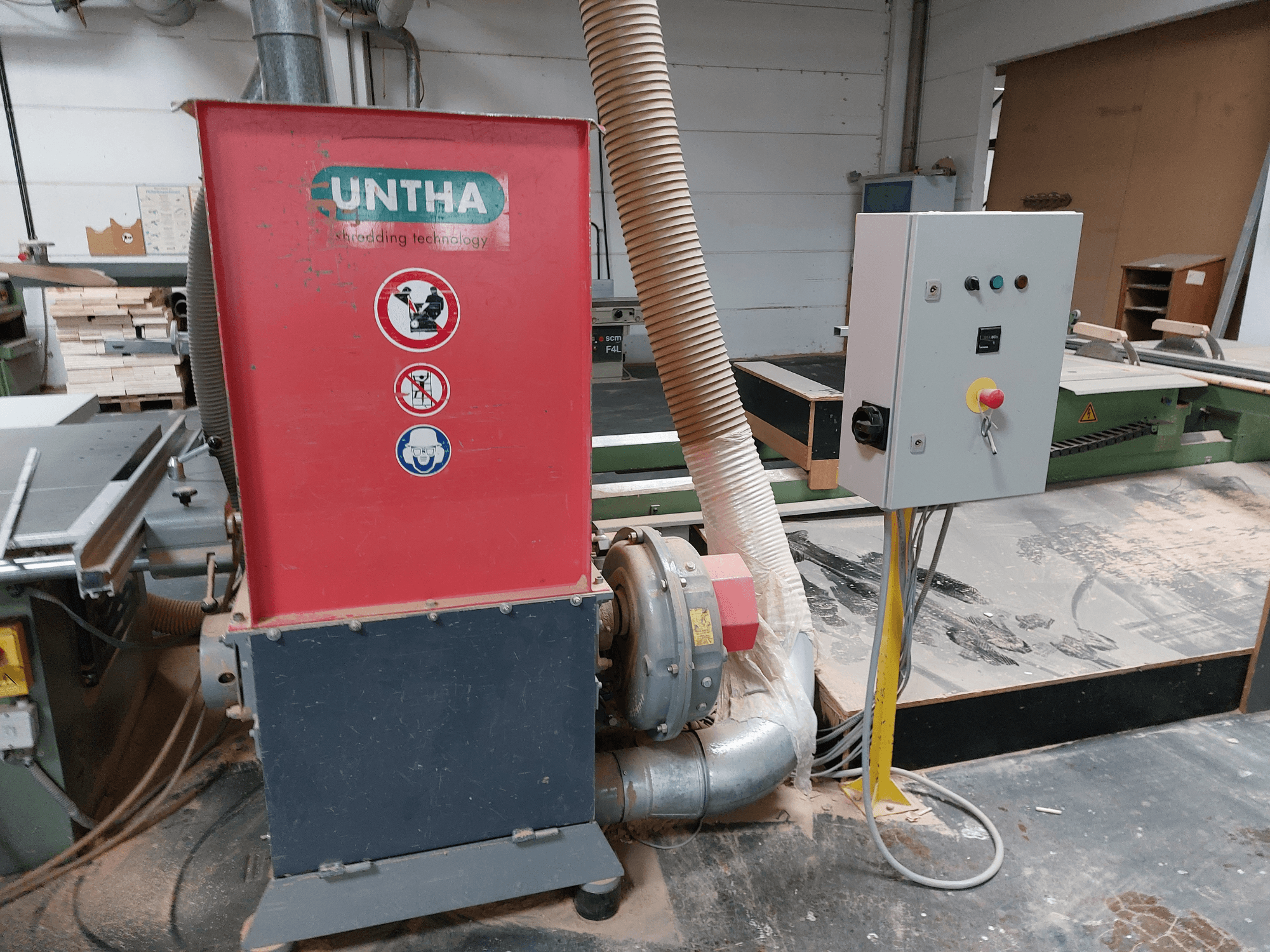 UNTHA wood shredder in red, side view; includes control panel with buttons and power switch, with dust collection hose.