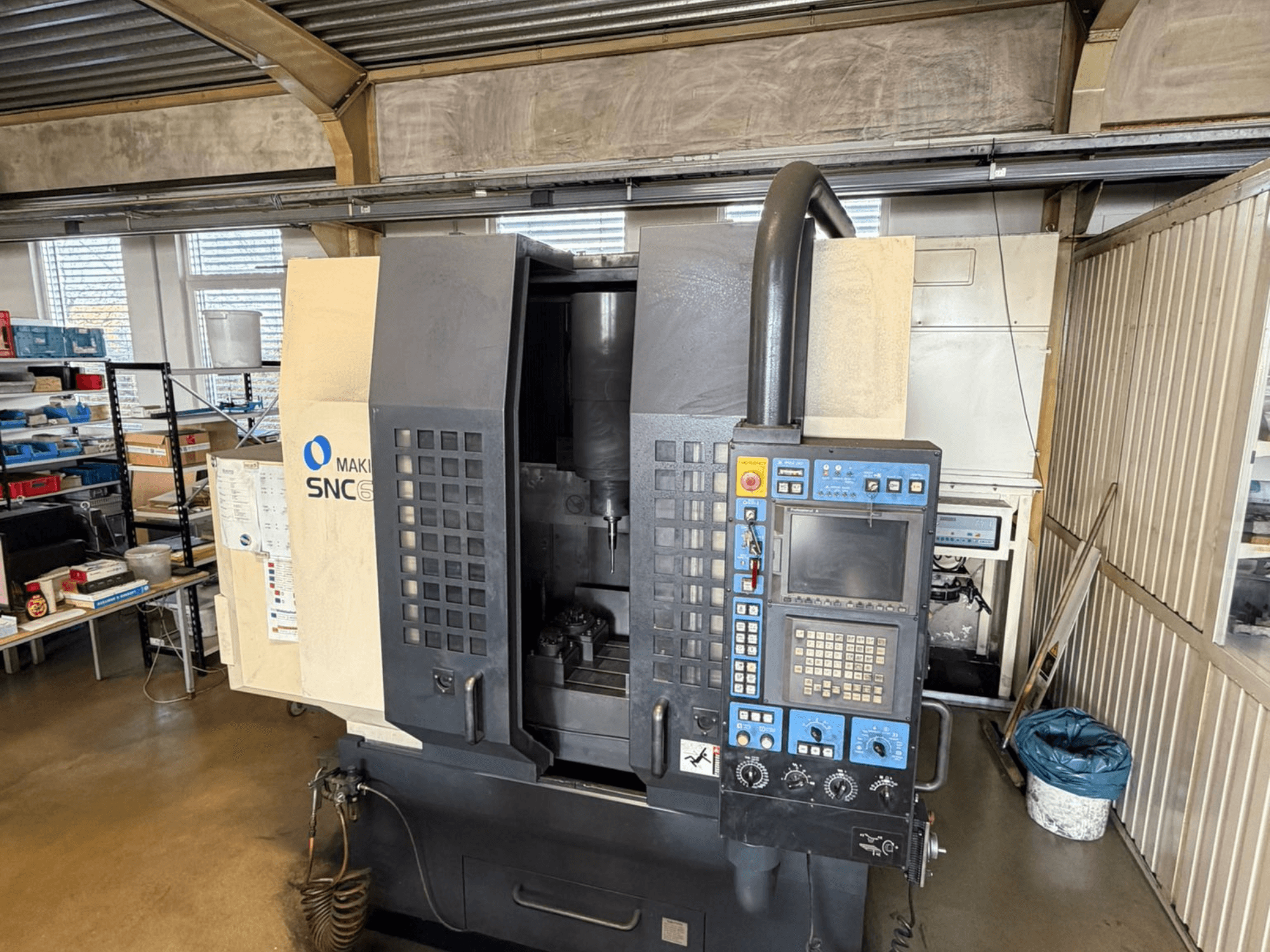 Makino SNC 64-A15 vertical machining center in front view, showcasing control panel, machining area, and industrial workspace.