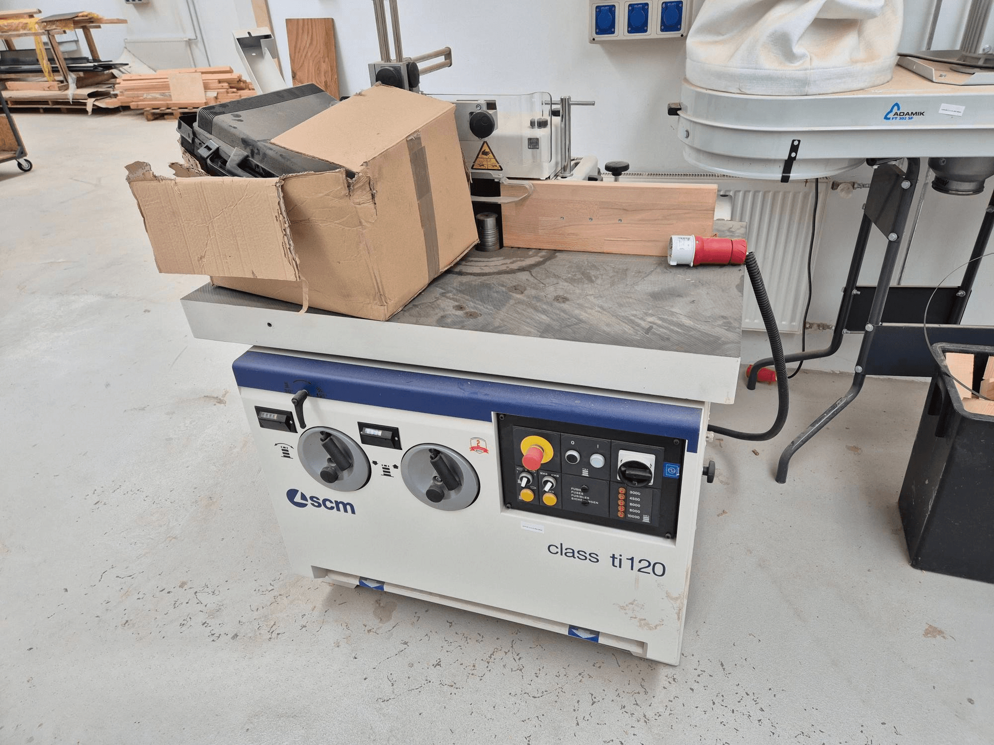 SCM class ti120 woodworking machine, front view, features a control panel with knobs and buttons, plus an attached cardboard box.