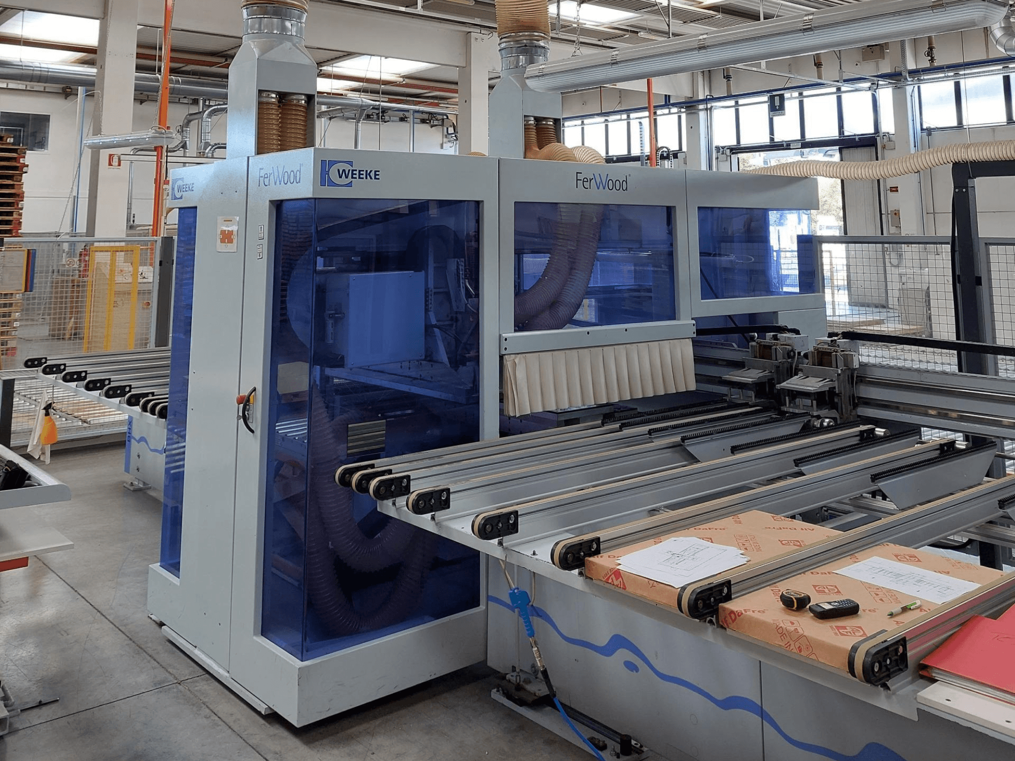Weeke FerWood CNC machine in a workshop, front view showing blue-tinted panels, control buttons, and worktable with materials.