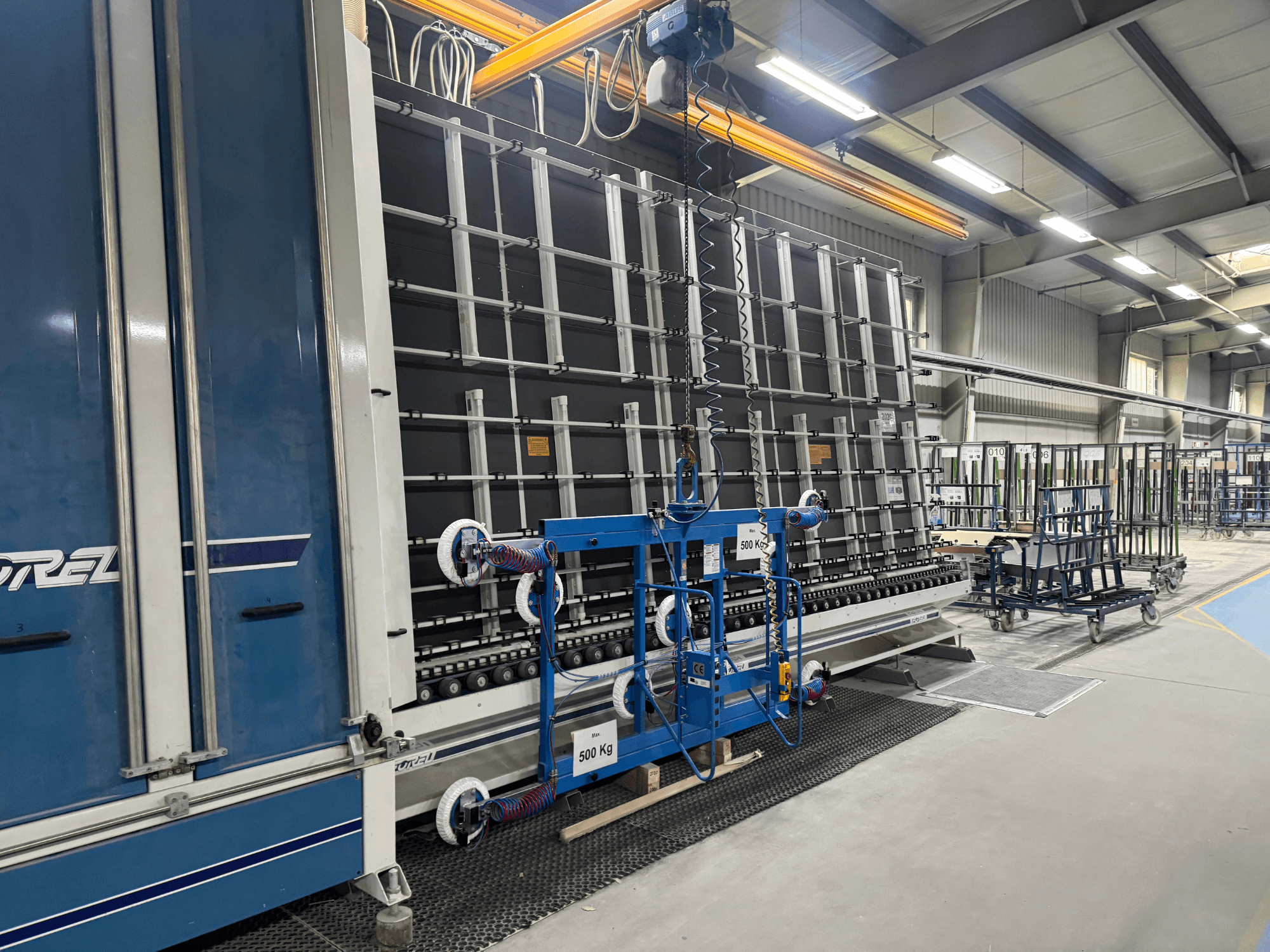 Industrial equipment by Drel, featuring a large frame and lifting mechanism, shown from a side view in a factory setting.