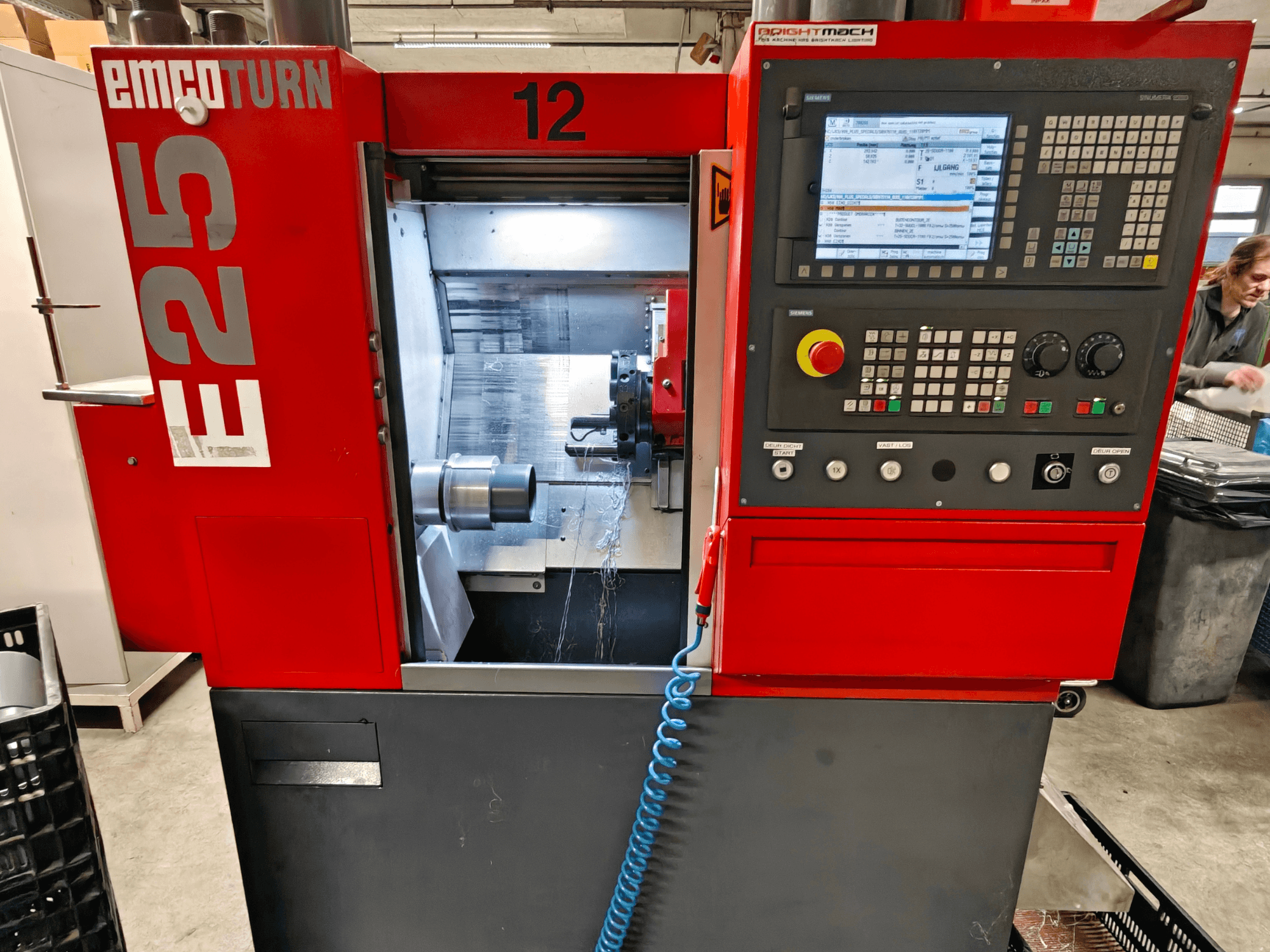EMCO TURN E25 machine front view, featuring control panel, tool holder, and interior area with cutting tool visible.