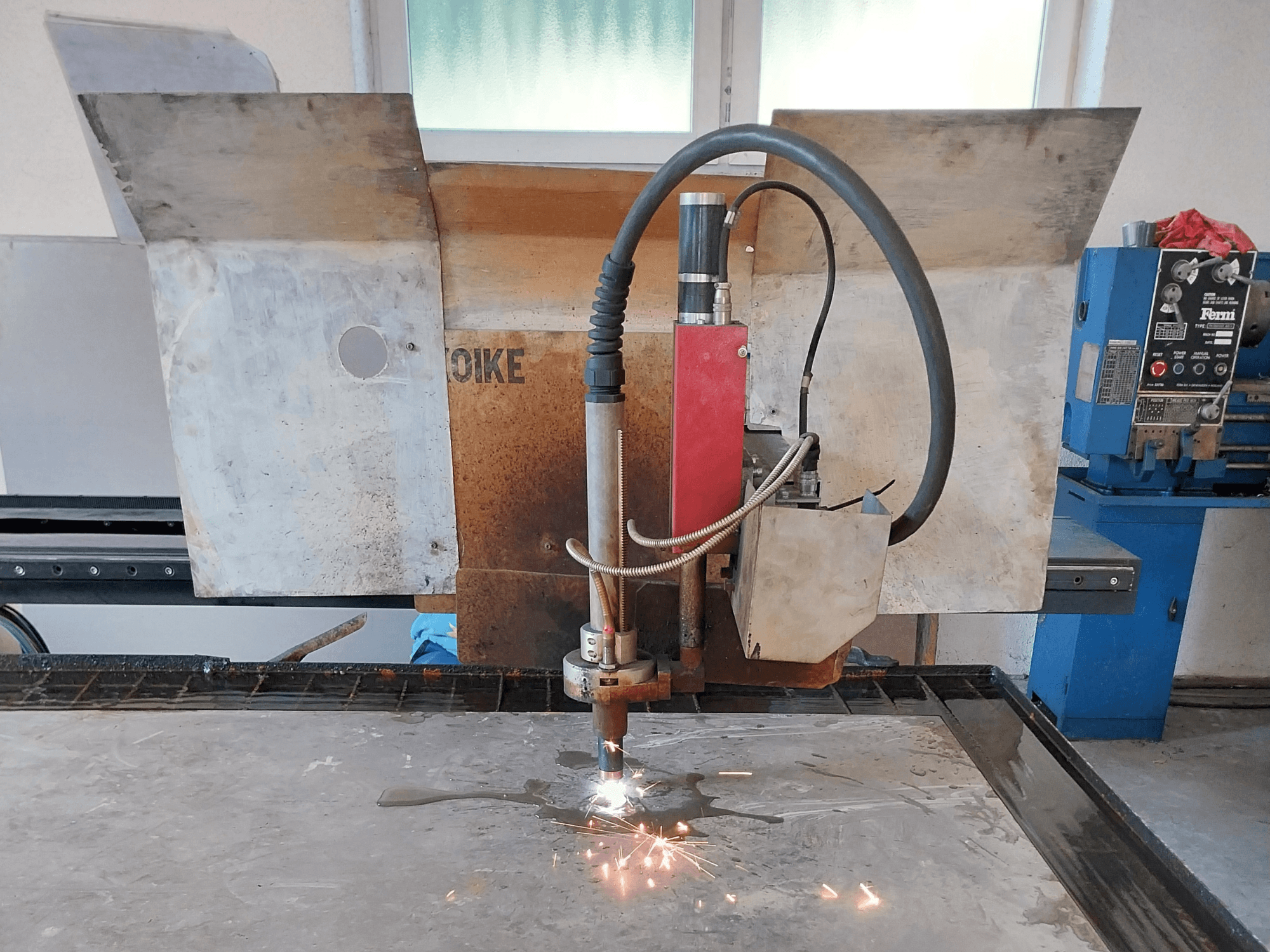 A front view of an Oike plasma cutter with sparks flying, positioned above a metal surface on a work table.