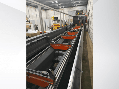 Industrial CNC machine side view, featuring linear rails, orange clamps, and precision components in a warehouse setting.