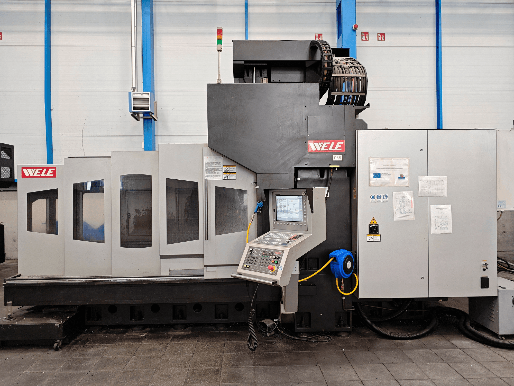 WELE machining center in a front view, featuring control panel, safety notices, and multiple access windows.