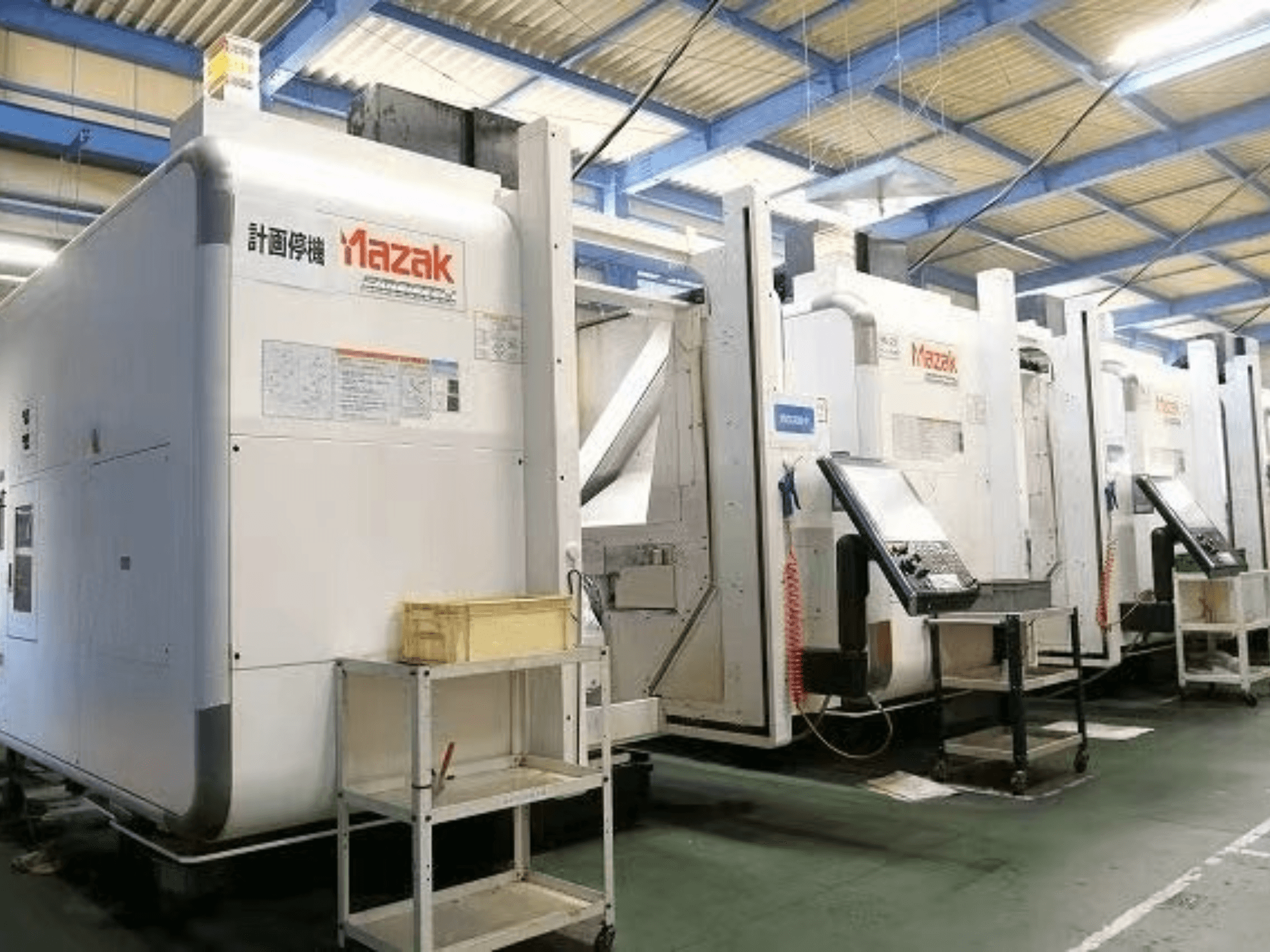 Mazak CNC machines in a factory setting, side view showcasing control panels and labels on white bodies.