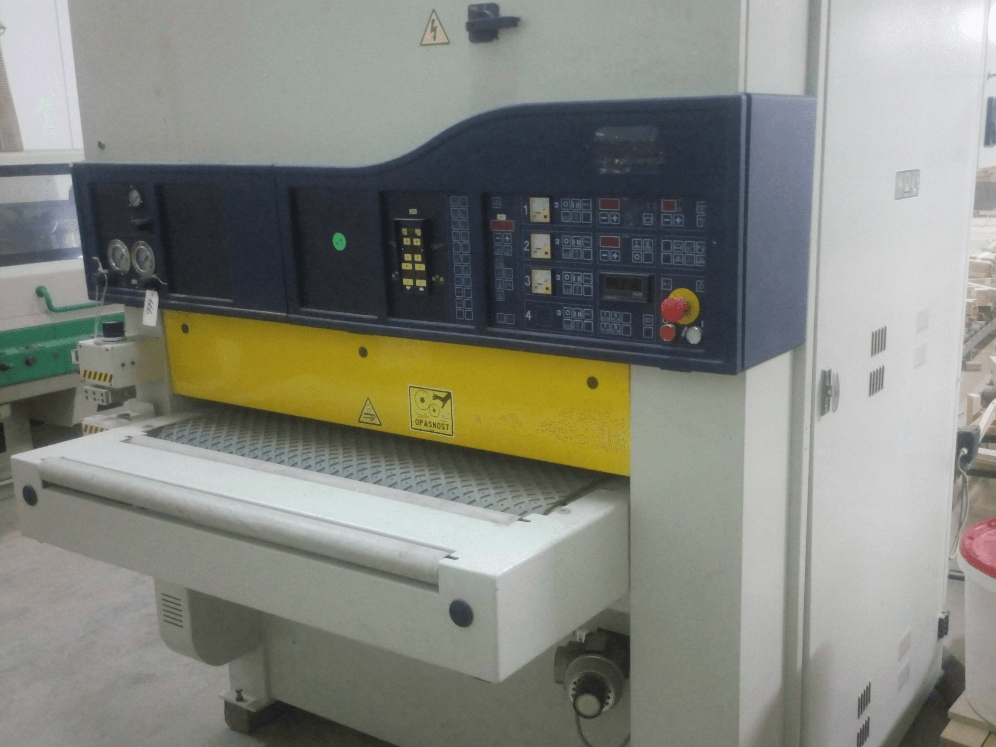 Industrial sanding machine with control panel, yellow and blue body, front view, showing gauges, switches, and conveyor surface.