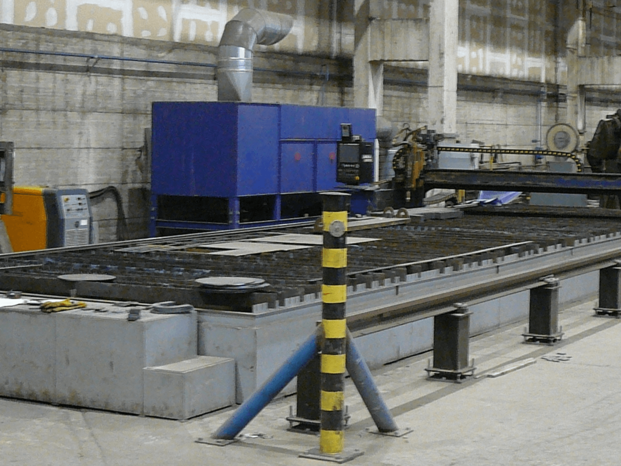 Industrial metal cutting machine setup, side view, featuring a blue control box, safety stripes, and metal work surface.