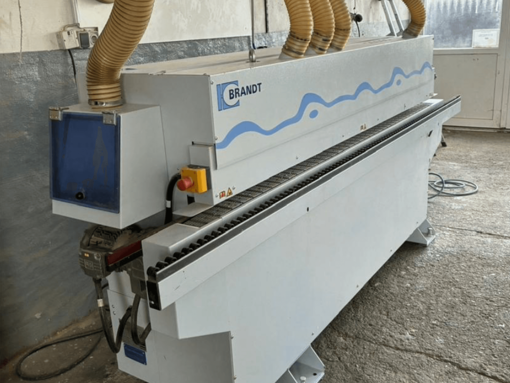 Brandt edge banding machine in front view with dust extraction hoses; features control panel and feed rollers.
