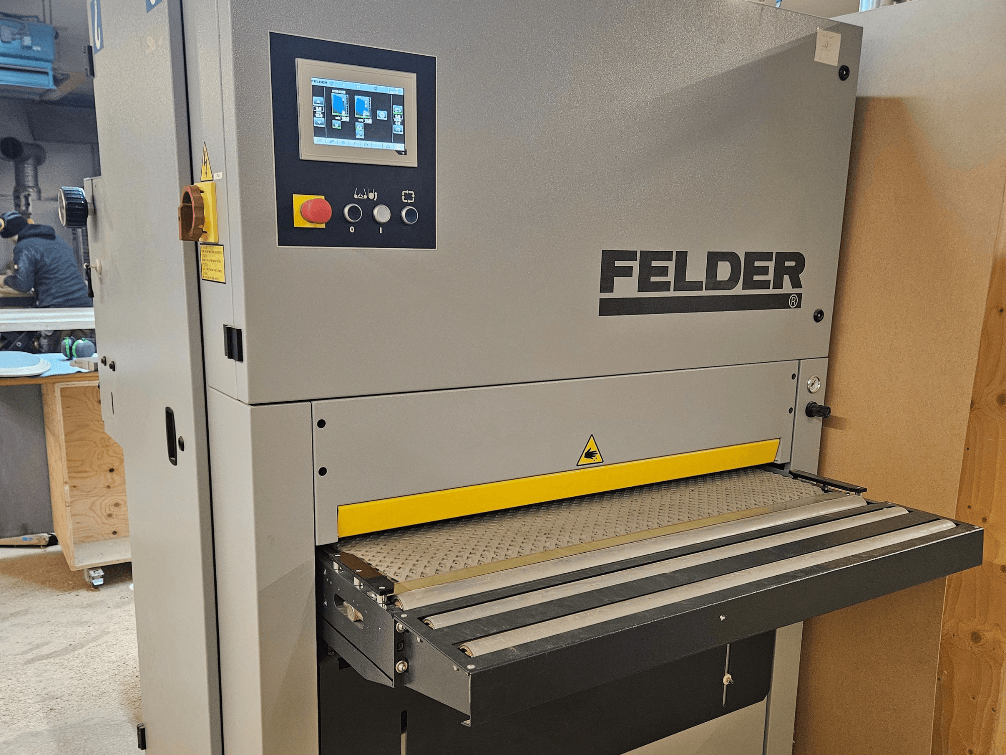 FELDER woodworking machine in a front view, featuring a digital control panel and yellow feed table with safety warnings.