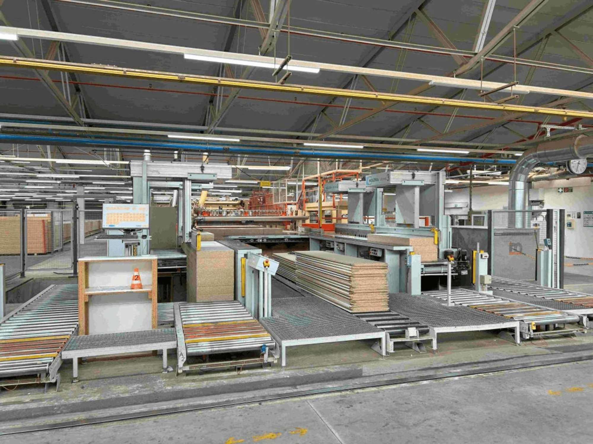 Manufacturing facility interior showing assembly lines with stacked panels and machinery, front view, bright lighting, modern equipment.