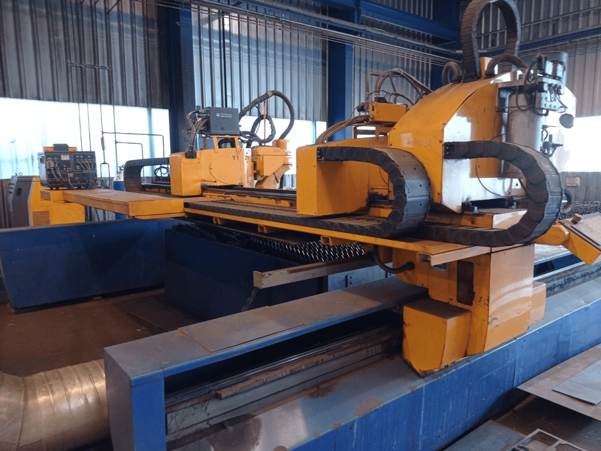Yellow CNC plasma cutting machine with two horizontal arms, shown from the front, featuring control panel and cutting bed.