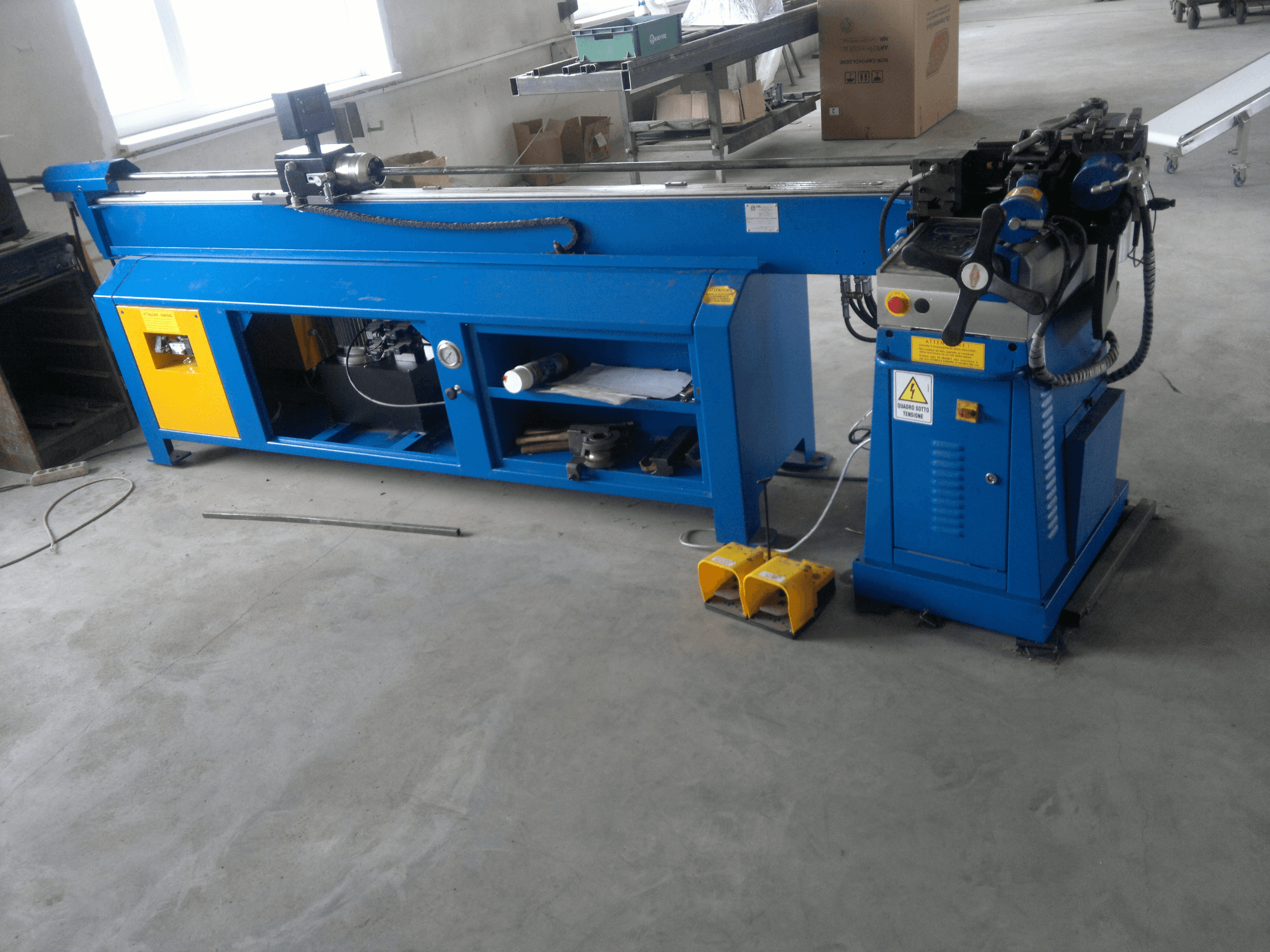 Blue woodworking machine with yellow accents, side view; features control panel, foot pedals, and a rotating blade assembly.