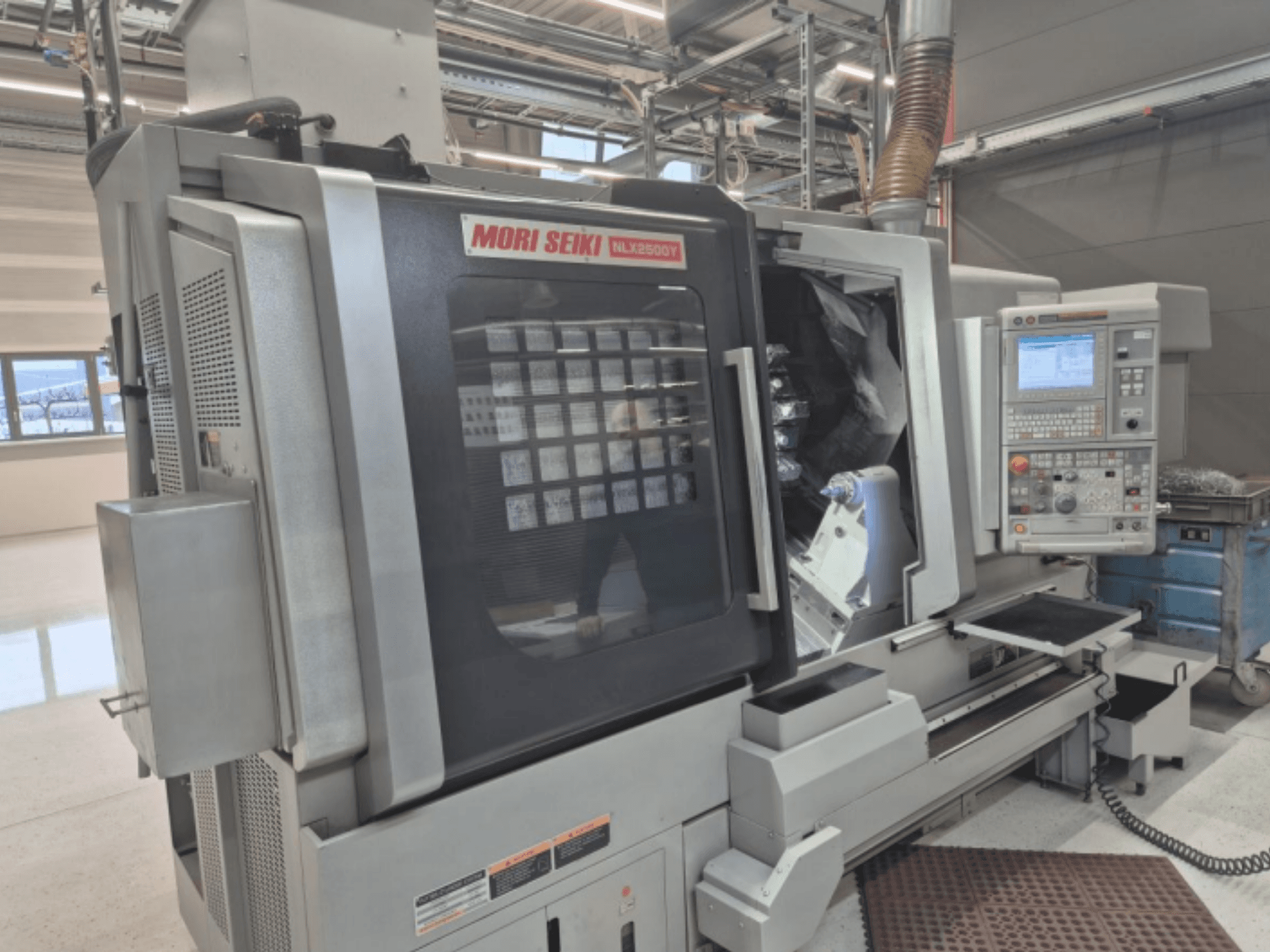 MORI SEIKI NL2500Y CNC lathe machine in a factory setting, front view displaying control panel and workpiece chamber.